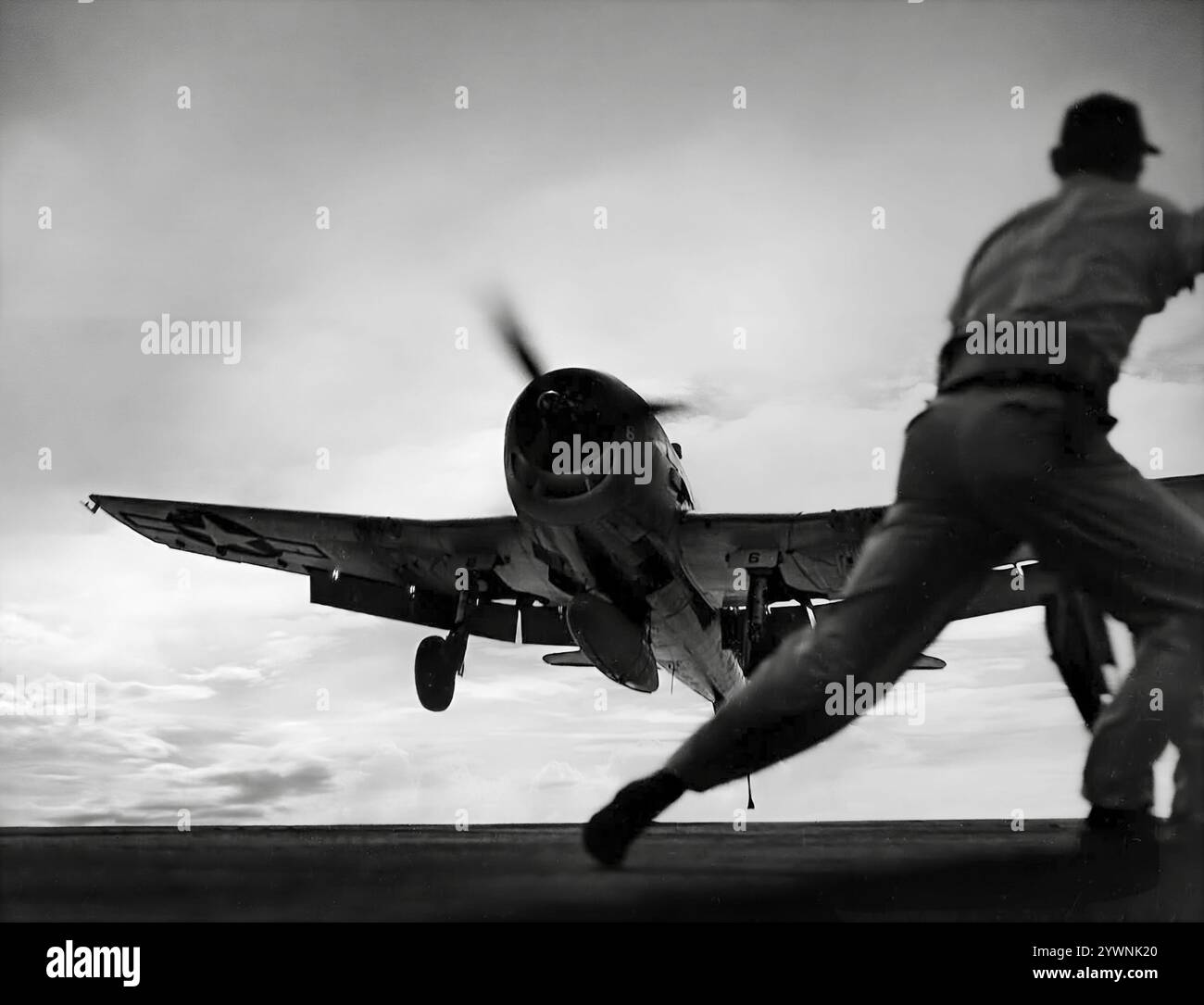Membre d'équipage maritime aidant à l'atterrissage d'un Grumman F6F Hellcat sur le pont d'envol du transporteur. Chasseur américain de la seconde Guerre mondiale, il a été conçu pour remplacer le F4F Wildcat et contrer le Mitsubishi A6M Zero japonais. L'avion a fait ses débuts au combat en septembre 1943 et s'est par la suite imposé comme un chasseur robuste et bien conçu et est devenu le chasseur dominant de l'United States Navy dans la seconde moitié de la guerre du Pacifique. Au total, 12 275 ont été construits en un peu plus de deux ans et les Hellcats ont été crédités de la destruction d'un total de 5 223 avions ennemis. Banque D'Images