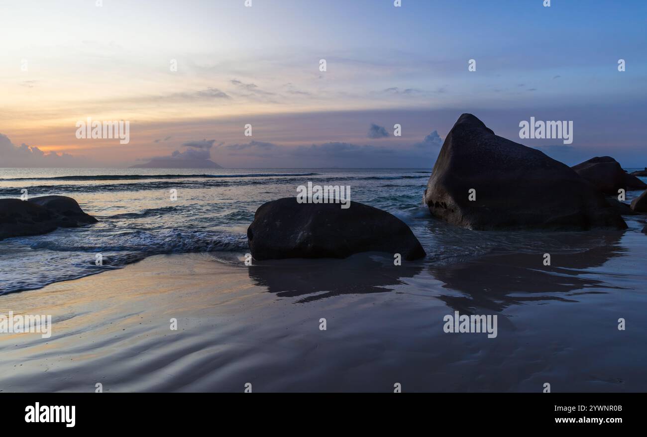 Beau Vallon Beach paysage avec sable humide et silhouettes de rochers côtiers sur le coucher du soleil. Île de Mahé, Seychelles Banque D'Images