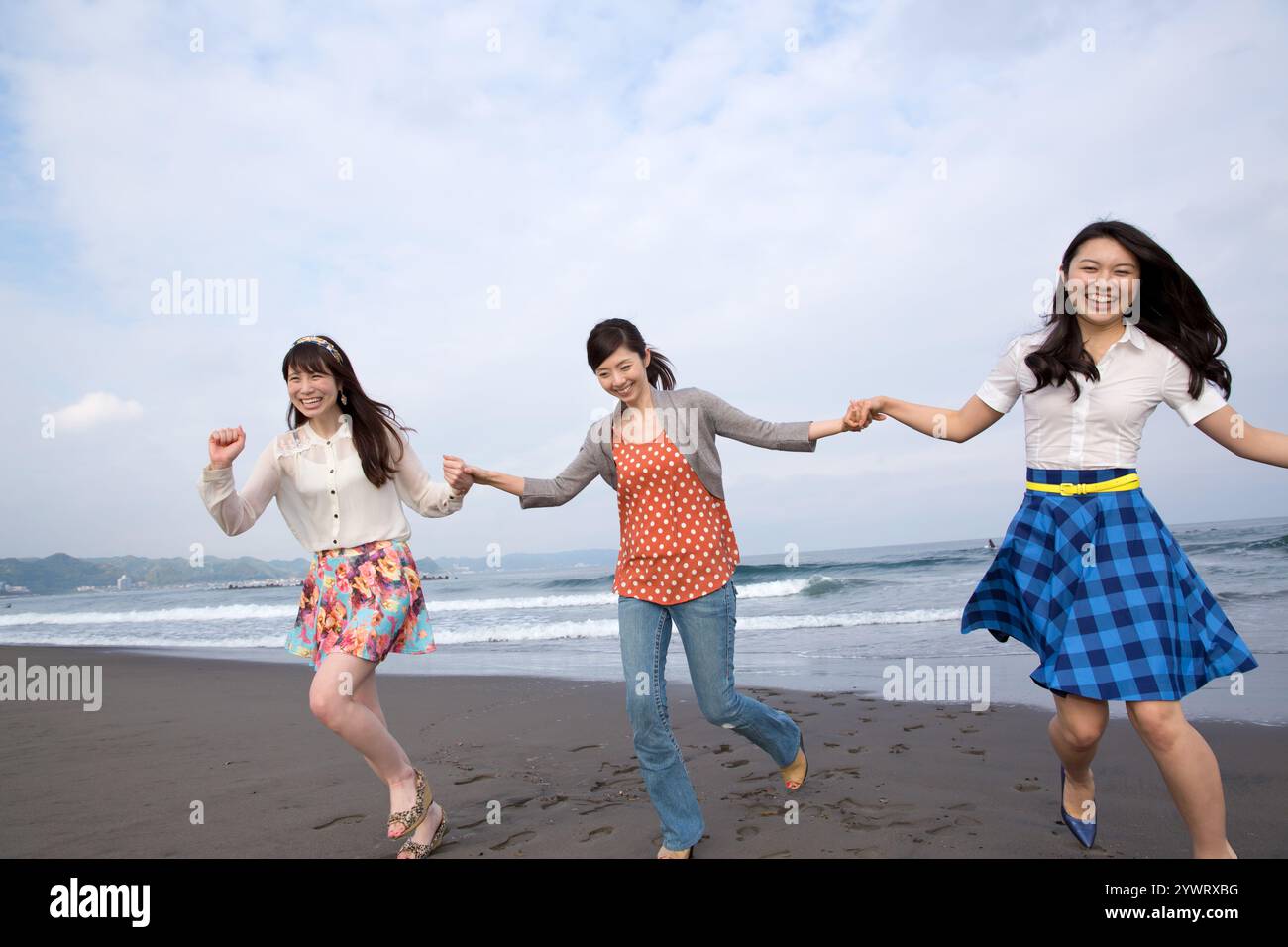 Trois jeunes femmes courant sur la plage de sable, se tenant par la main Banque D'Images