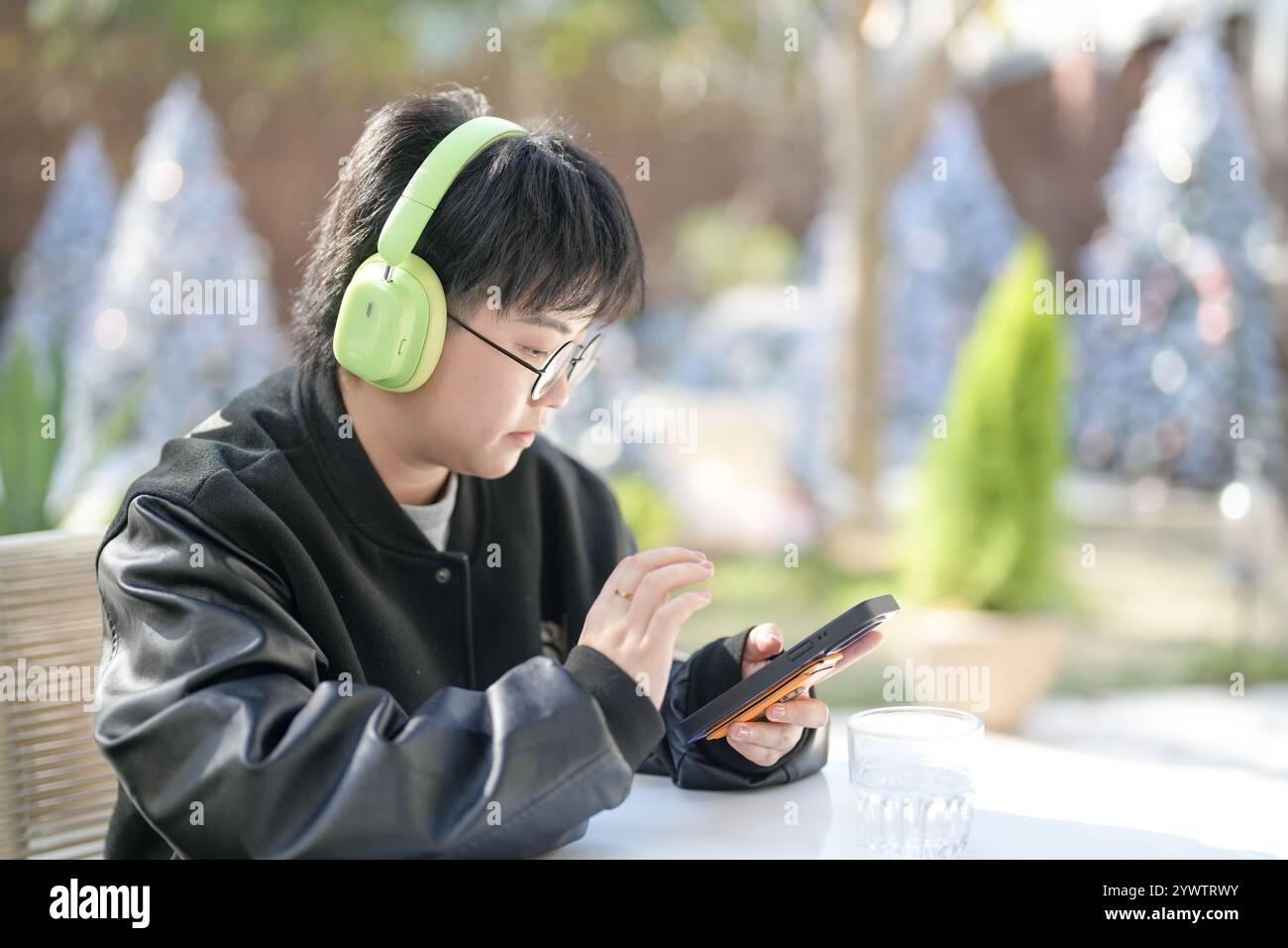 Une femme chinoise dans les années 30 en vêtements sportifs utilise un smartphone tout en écoutant de la musique à travers des écouteurs à une table dans un café élégant sur Jilu Ro Banque D'Images