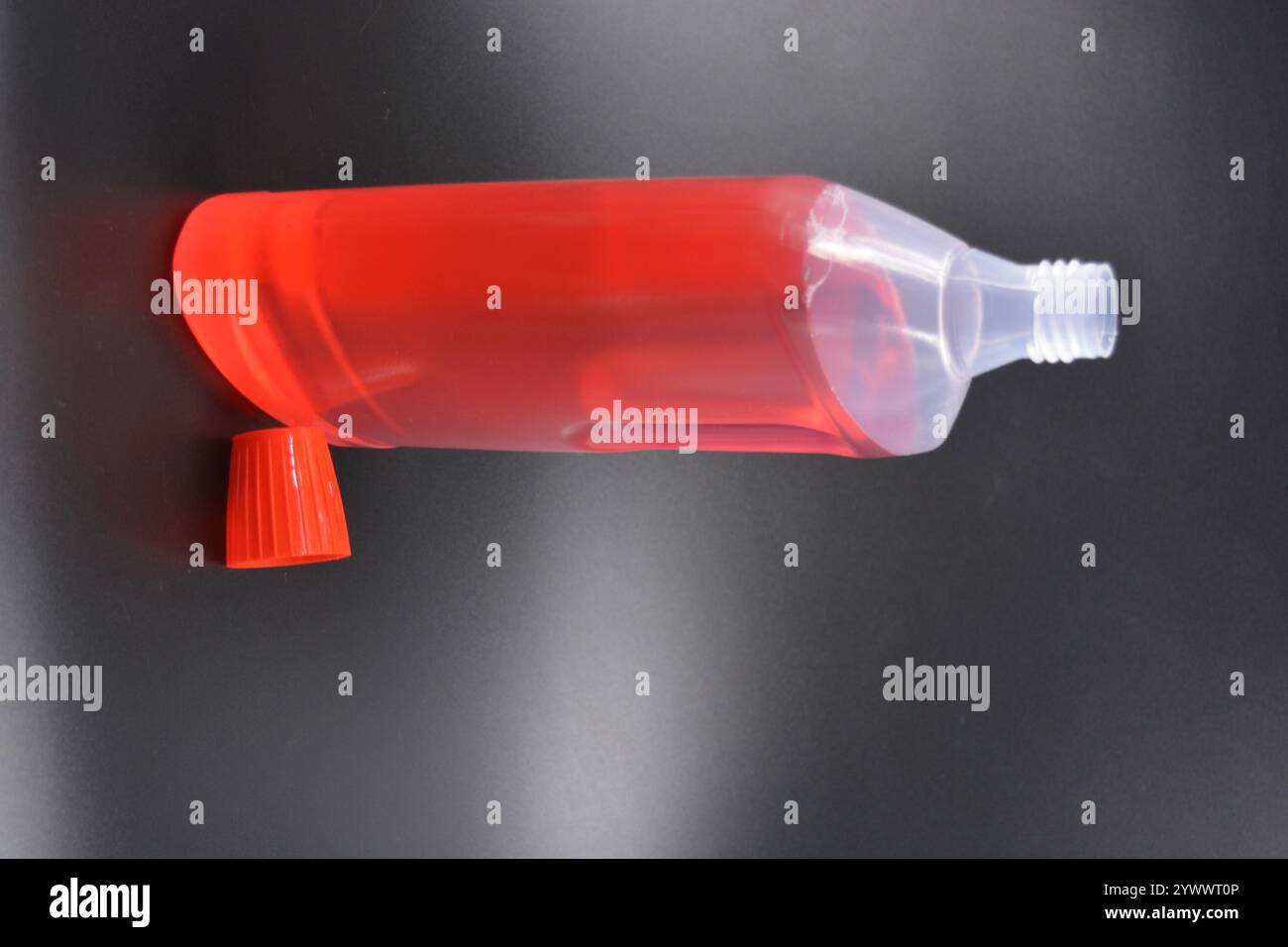 Une grande bouteille transparente pour laver les vêtements, le linge de lit, les tissus et les salles de nettoyage. Une bouteille en plastique remplie d'un liquide rouge avec un bouchon rouge vif Banque D'Images