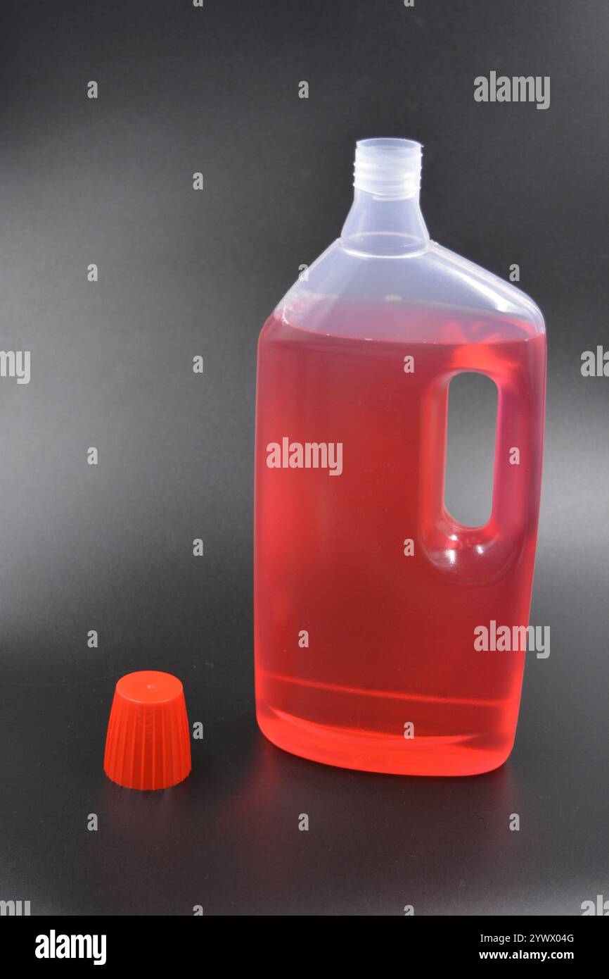 Une grande bouteille transparente pour laver les vêtements, le linge de lit, les tissus et les salles de nettoyage. Une bouteille en plastique remplie d'un liquide rouge avec un bouchon rouge vif Banque D'Images