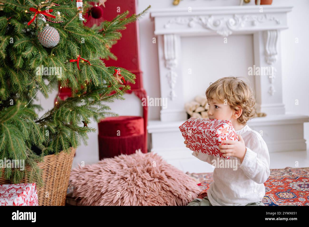 Enfant excité tenant un cadeau devant un sapin de Noël joliment décoré pendant la saison des fêtes Banque D'Images