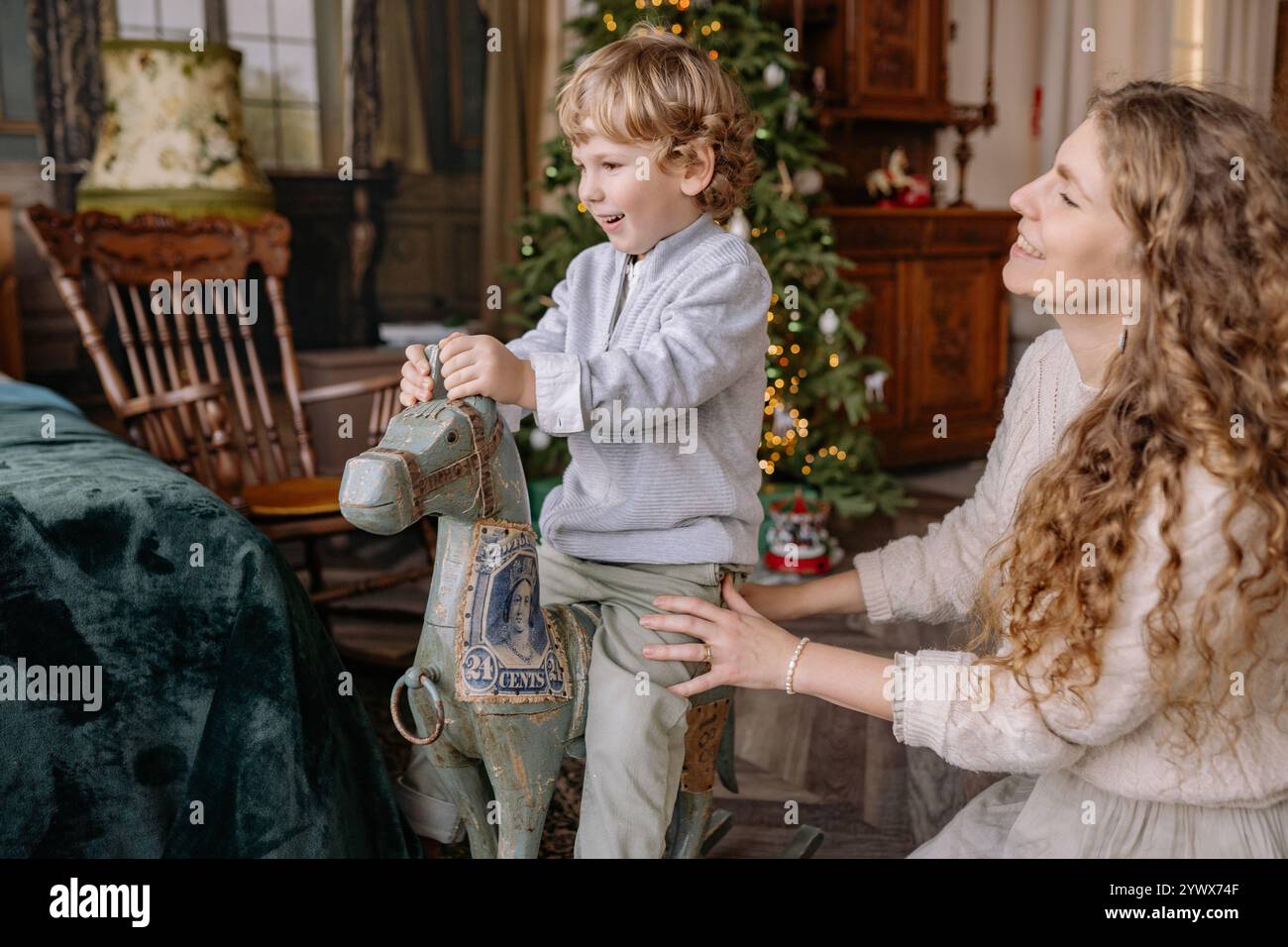 Enfant profitant de Noël avec sa mère, monter un cheval à bascule vintage dans une chambre de vacances confortable Banque D'Images