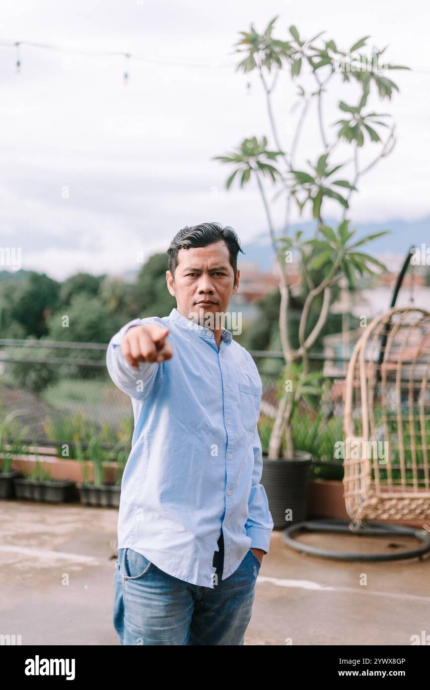 Un homme d'Asie du Sud-est montrant de la frustration, pointant vers l'avant avec une expression intense, capturant une émotion de colère ou de désaccord. Banque D'Images
