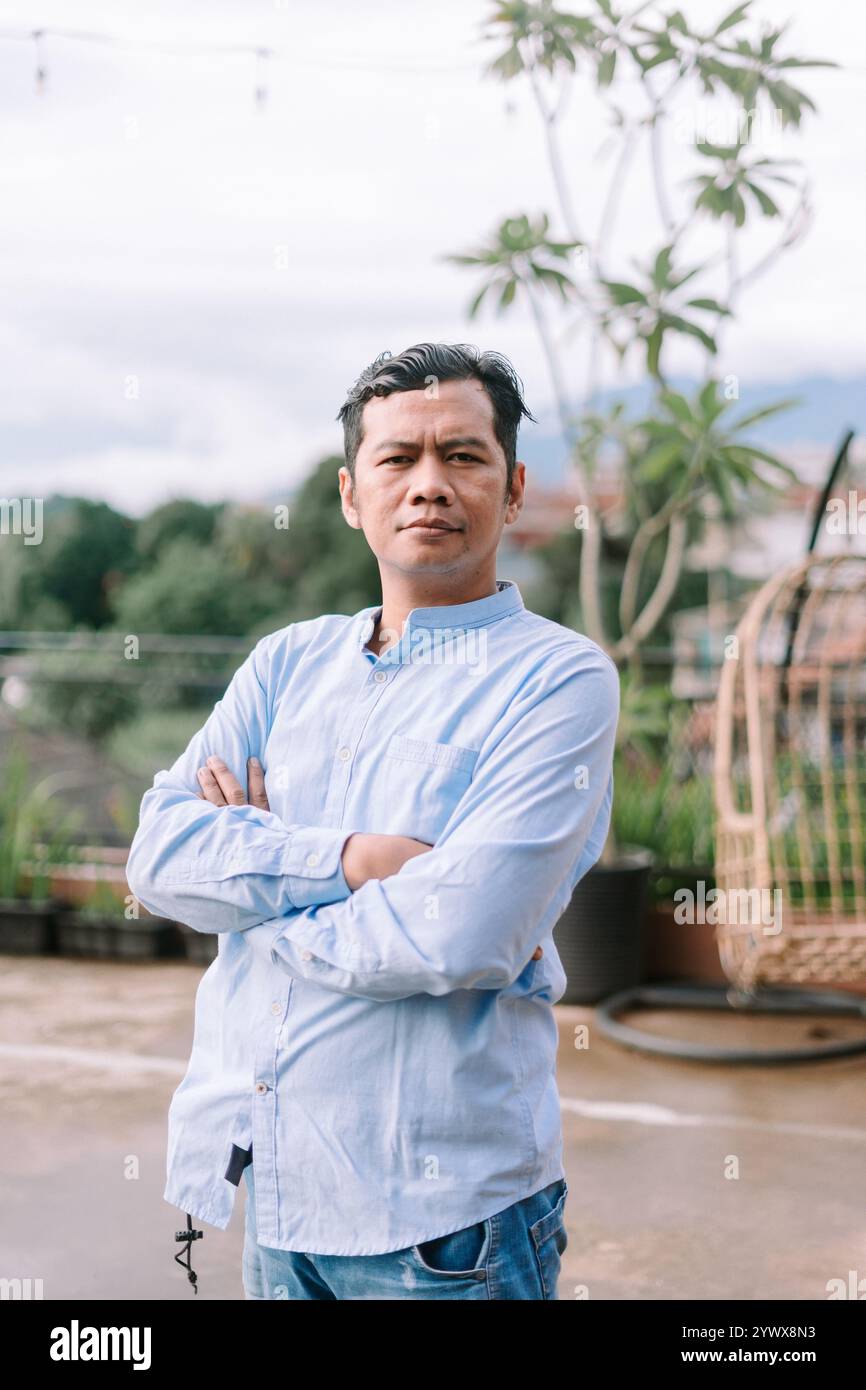 Un homme d'Asie du Sud-est croisant les bras, affichant une position réfléchie ou confiante, idéal pour les thèmes de contemplation, d'attitude ou d'affirmation de soi Banque D'Images