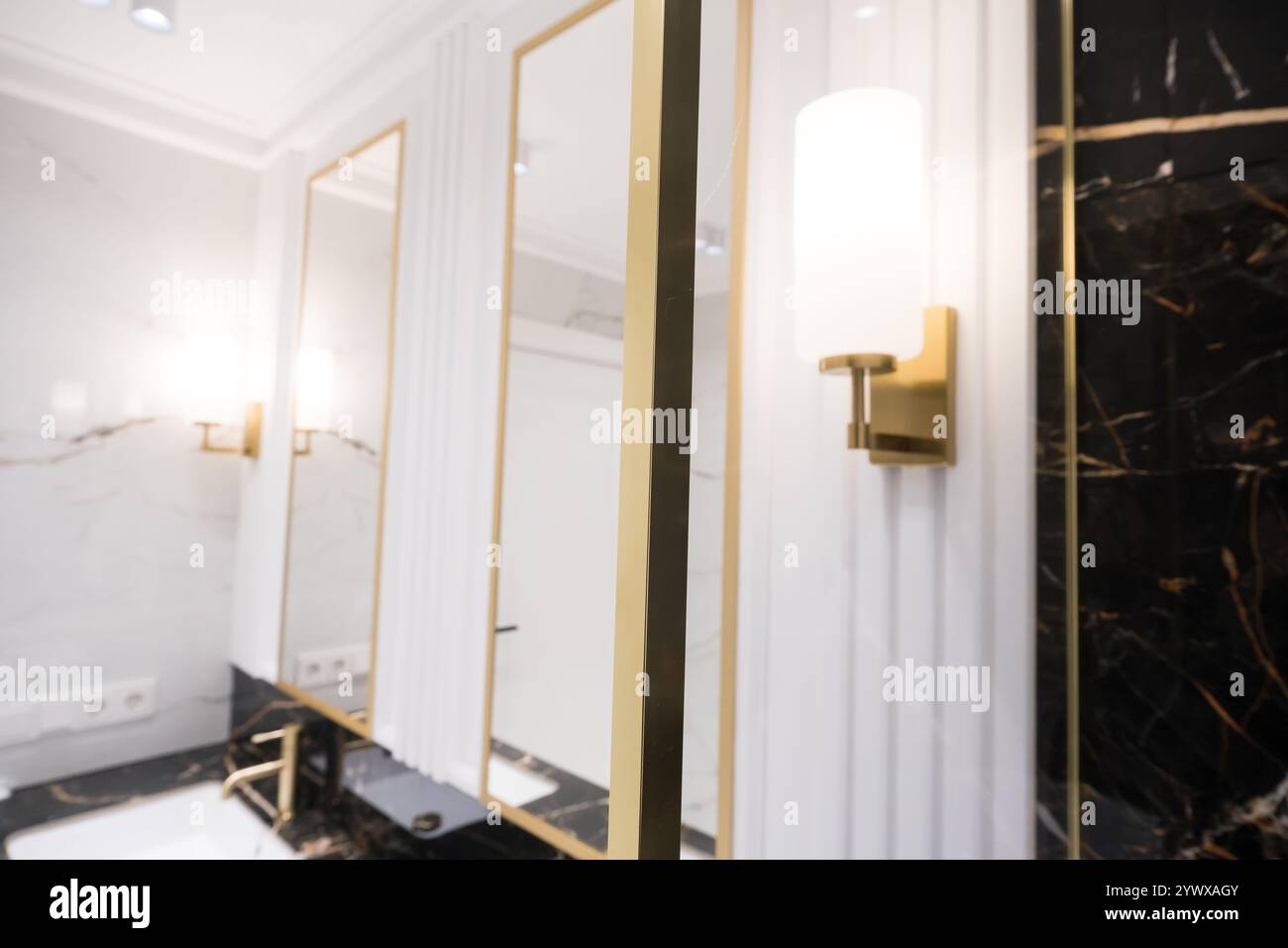Une salle de bains avec des carreaux de métro verticaux en marbre et empilés, un meuble-lavabo en chêne blanc, des miroirs carrés encadrés de noir et des robinets, et un comptoir en marbre. Banque D'Images