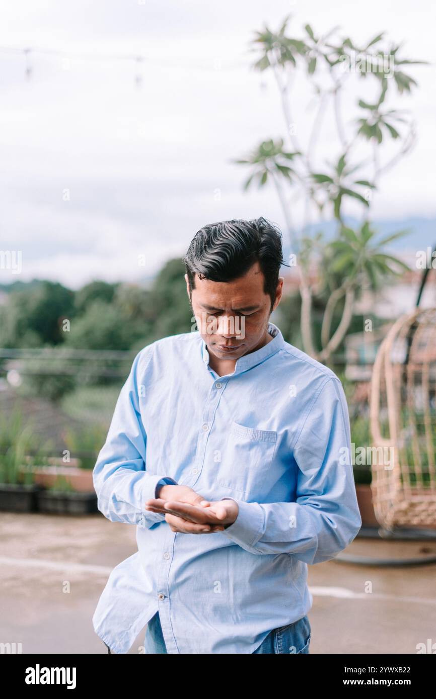 Un homme d'Asie du Sud-est regardant sa paume, profondément dans la pensée ou la curiosité, capturant un moment de réflexion ou d'auto-apprentissage Banque D'Images