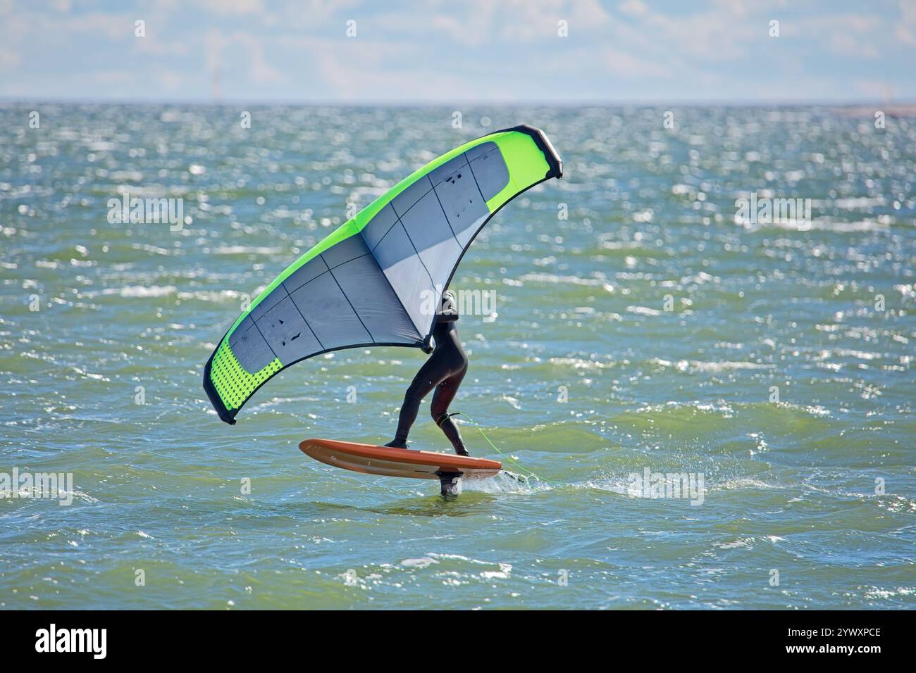 L'homme joue l'aile en utilisant l'aile gonflable portative et la planche de surf hydrofoil en mer en été. Cavalier sur une planche d'aile de vent, surfe les vagues. Banque D'Images