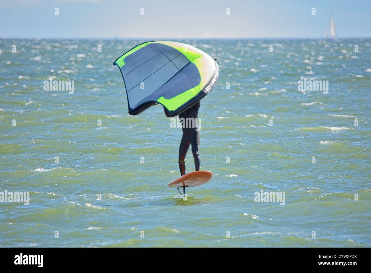 L'homme joue l'aile en utilisant l'aile gonflable portative et la planche de surf hydrofoil en mer en été. Cavalier sur une planche d'aile de vent, surfe les vagues. Banque D'Images