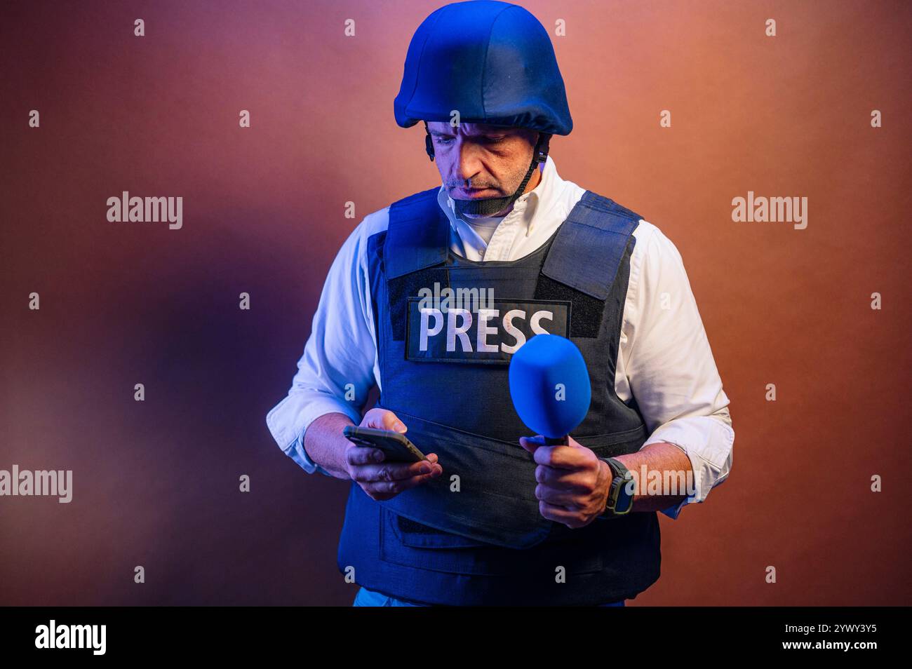 Reporter en gilet pare-balles tenant un microphone et un smartphone en studio. Banque D'Images