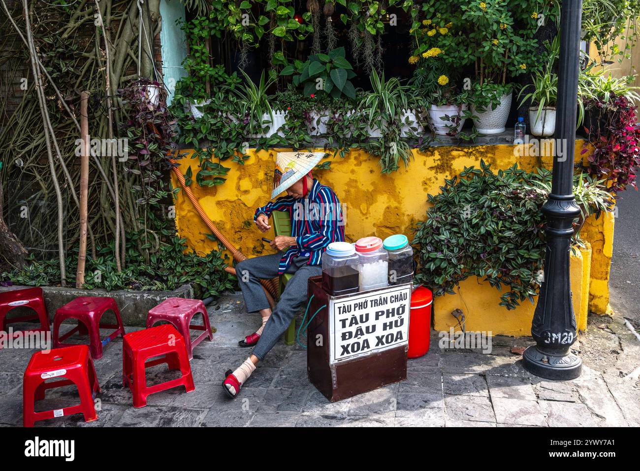 Vietnam, Hoi an, 2024-02-19, vieille ville, magasin de rue, vendeur au repos, petit tabouret en plastique rouge, chapeau de paille vietnamien, vie de rue, chaleur, soleil Banque D'Images