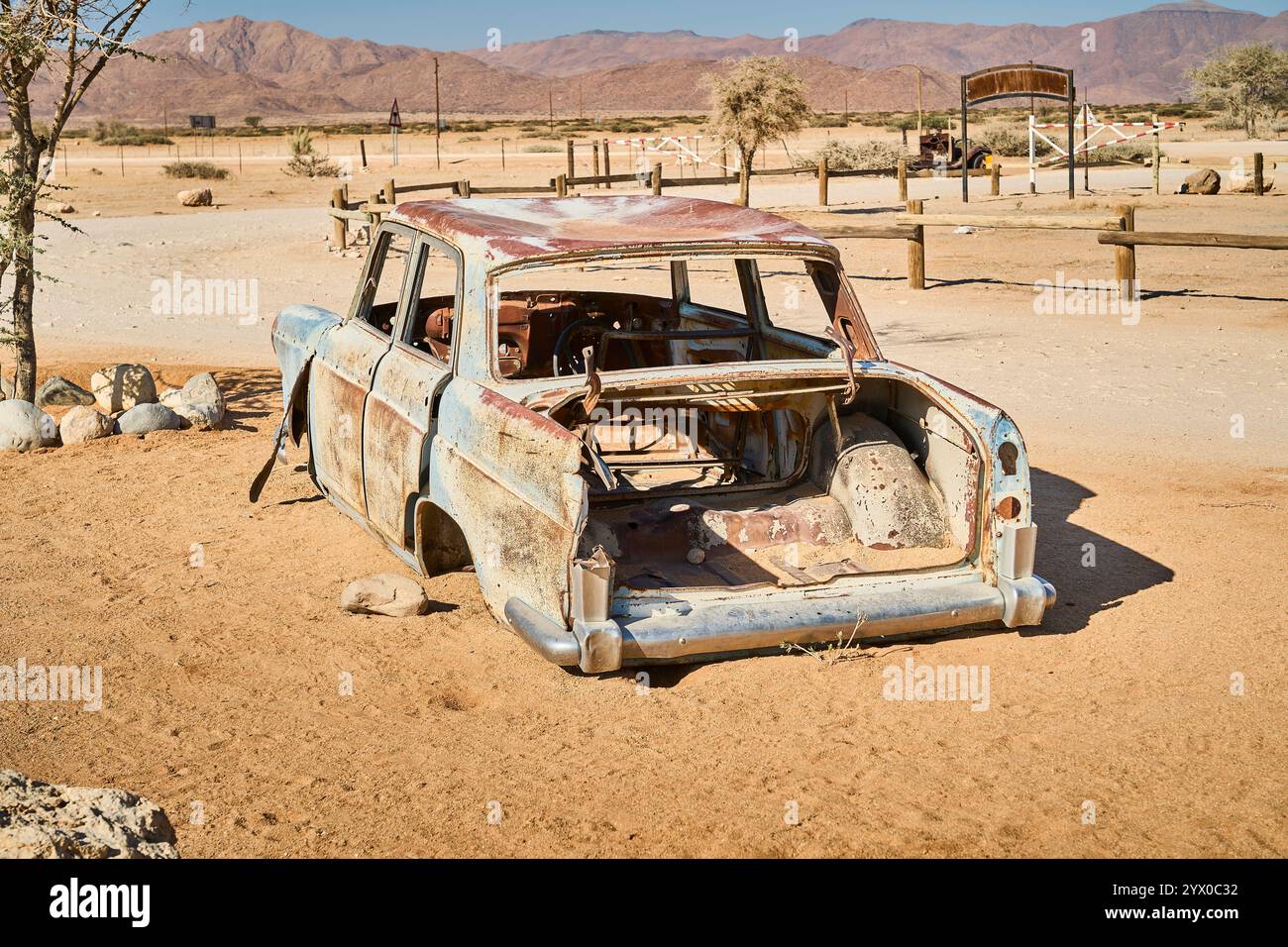 La carcasse dépouillée et rouillée d'une voiture de collection est abandonnée dans le terrain sablonneux de Solitaire, en Namibie, avec des montagnes du désert en arrière-plan. Banque D'Images