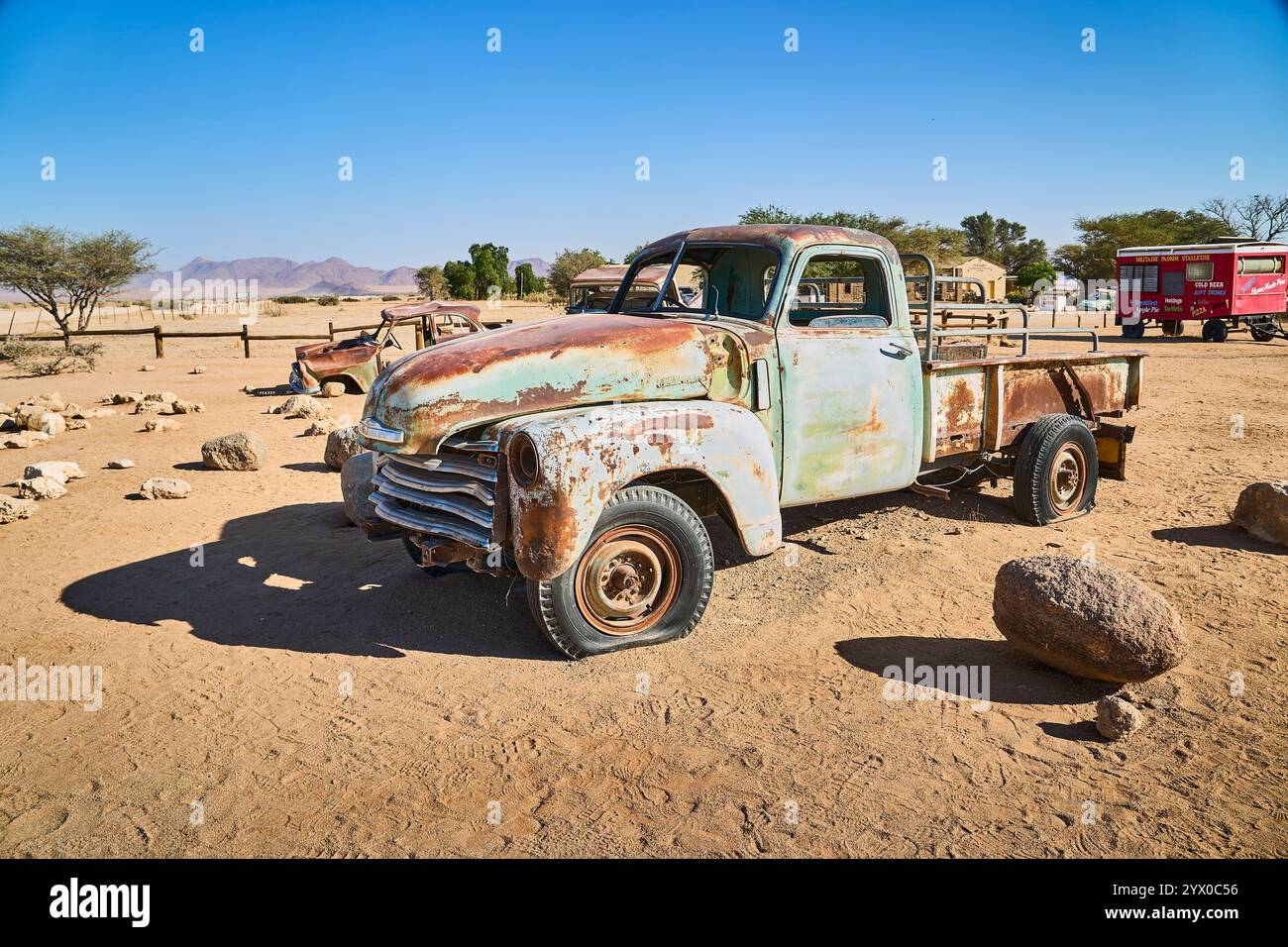Un vieux pick-up rouillé avec des pneus à plat se tient abandonné sur le sol sablonneux de Solitaire, Namibie, sous un ciel bleu désert éclatant. Banque D'Images
