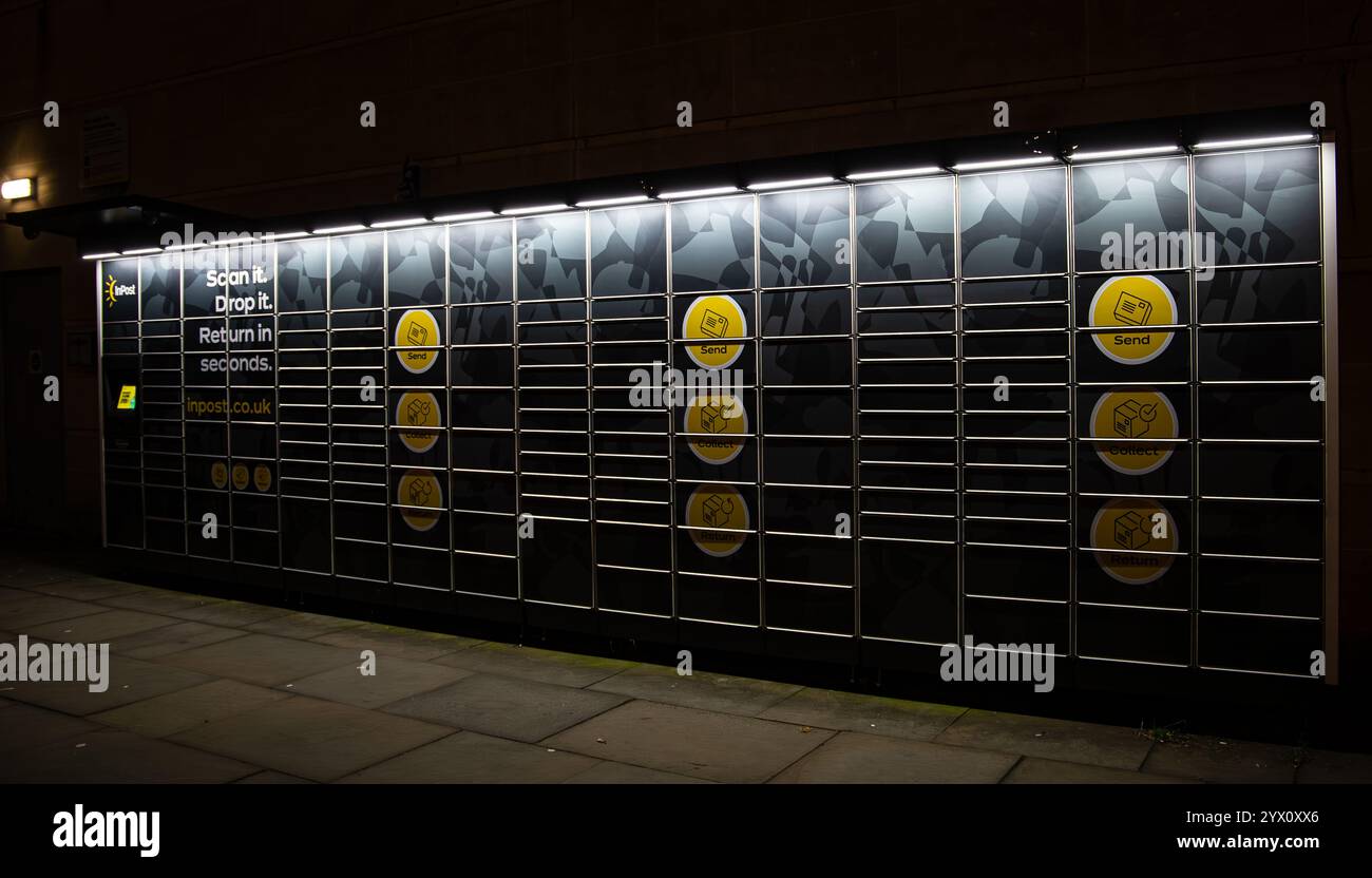 Un mur de casier à colis sombre et éclairé sur une rue avec des cercles jaunes marqués et des instructions textuelles pour numériser et déposer Banque D'Images