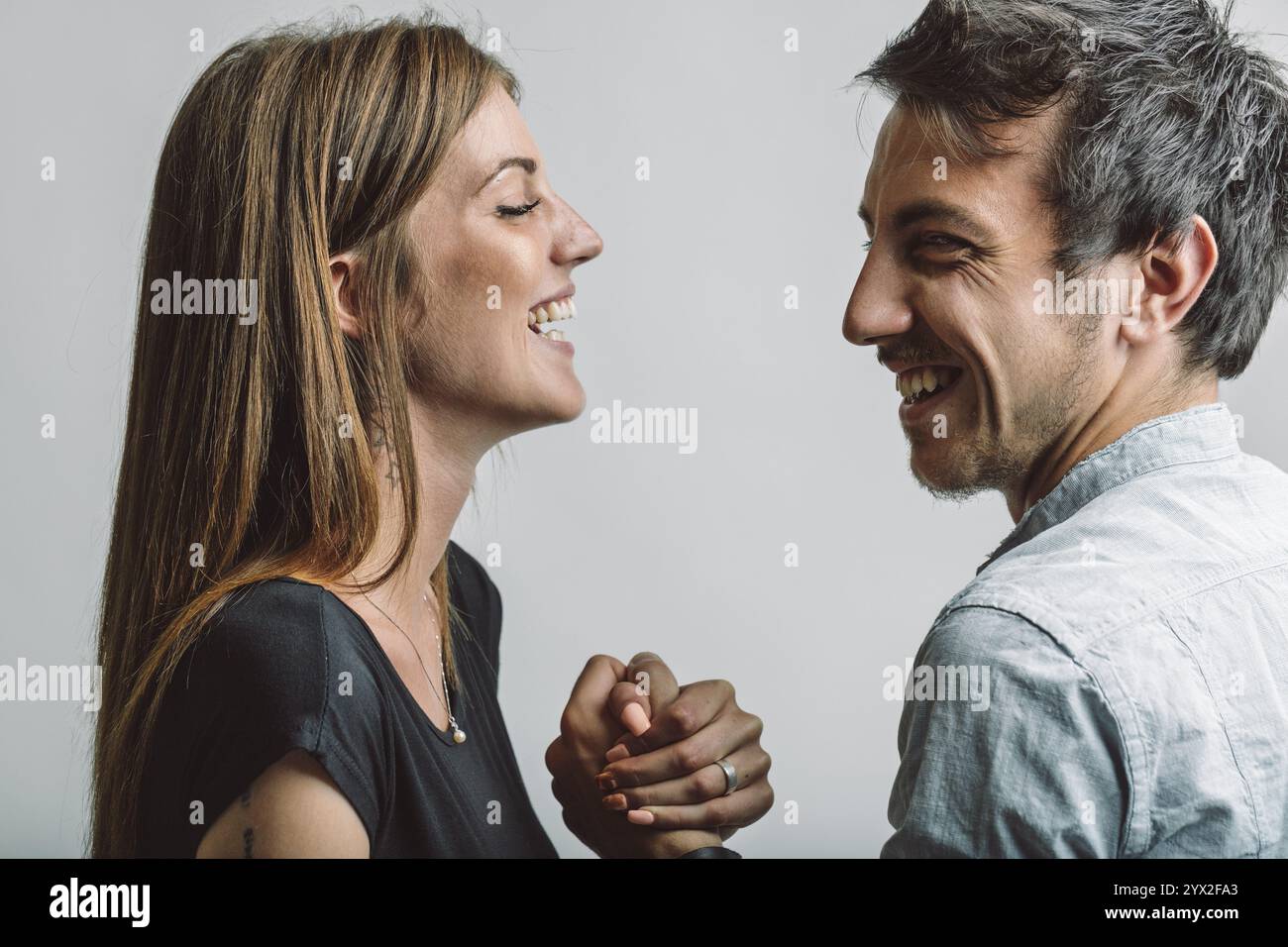 Prise de vue studio mettant en scène un jeune couple souriant et se tenant par la main, rayonnant d’affection et de complicité tout en profitant à nouveau d’un moment de joie et de connexion Banque D'Images