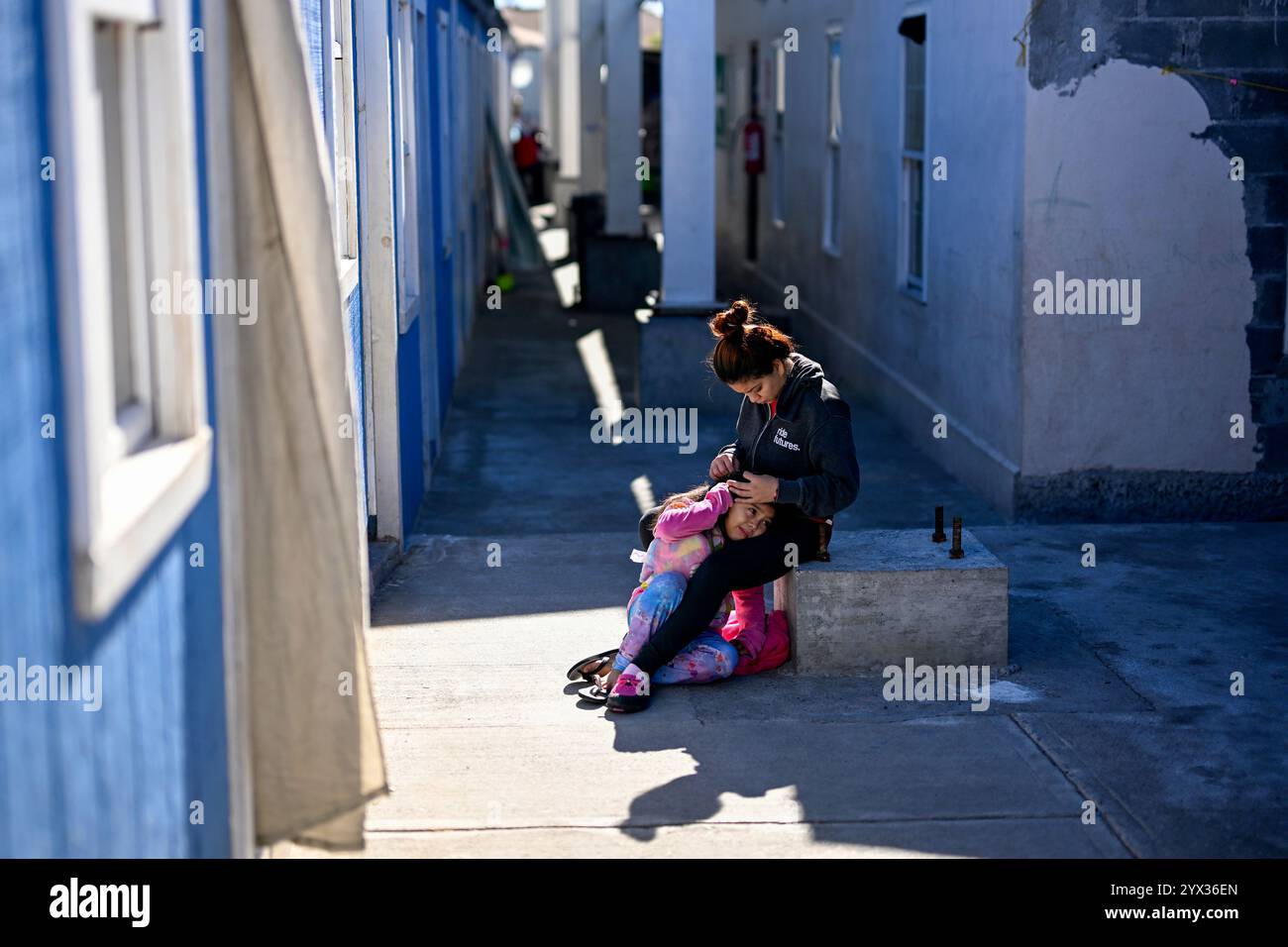 Reynosa, Mexique. 11 décembre 2024. Une migrante fixe les cheveux d'une jeune fille dans un refuge de la ville frontalière de Reynosa, Tamaulipas, Mexique, 11 décembre 2024. Reynosa, une ville frontalière de Tamaulipas, se trouve de l'autre côté du Rio Grande de McAllen, Texas des États-Unis. En raison de sa situation géographique, Reynosa sert de porte d'entrée majeure pour les migrants d'Amérique centrale et d'autres régions qui tentent d'entrer aux États-Unis. Les refuges de cette région fournissent un logement temporaire aux migrants en attente de demandes d'asile, de permis de transit ou de retour dans leur foyer. Crédit : Li Muzi/Xinhua/Alamy Live News Banque D'Images