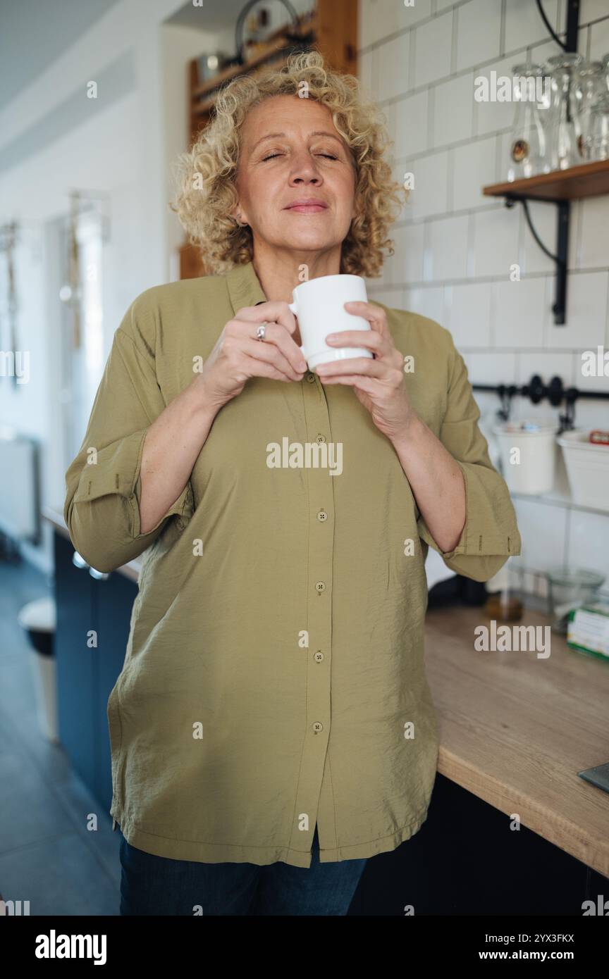 Femme d'âge moyen appréciant le café aromatique frais dans la cuisine. Banque D'Images