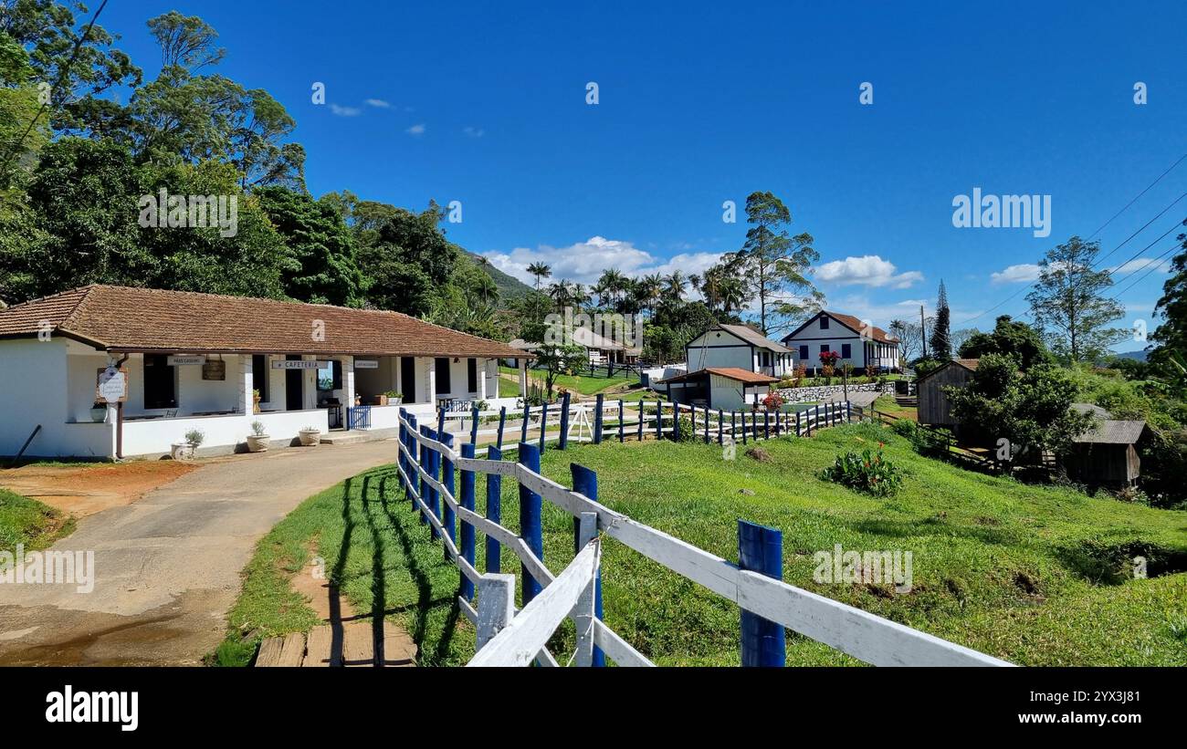 Un charmant bâtiment blanc avec un toit de tuiles se dresse à gauche, orné de signes simples et de plantes en pot, suggérant un café confortable ou un centre d'accueil. - Image de stock capturée avec un smartphone