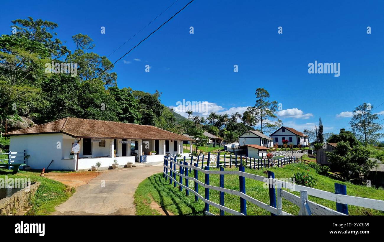 Un charmant bâtiment blanc avec un toit de tuiles se dresse à gauche, orné de signes simples et de plantes en pot, suggérant un café confortable ou un centre d'accueil. - Image de stock capturée avec un smartphone