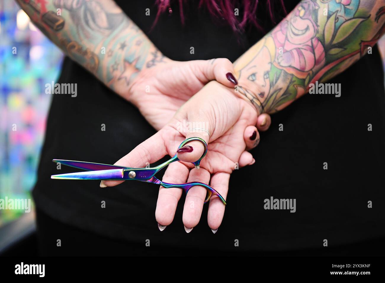 Gros plan de mains tatouées tenant des ciseaux colorés, artistique f Banque D'Images