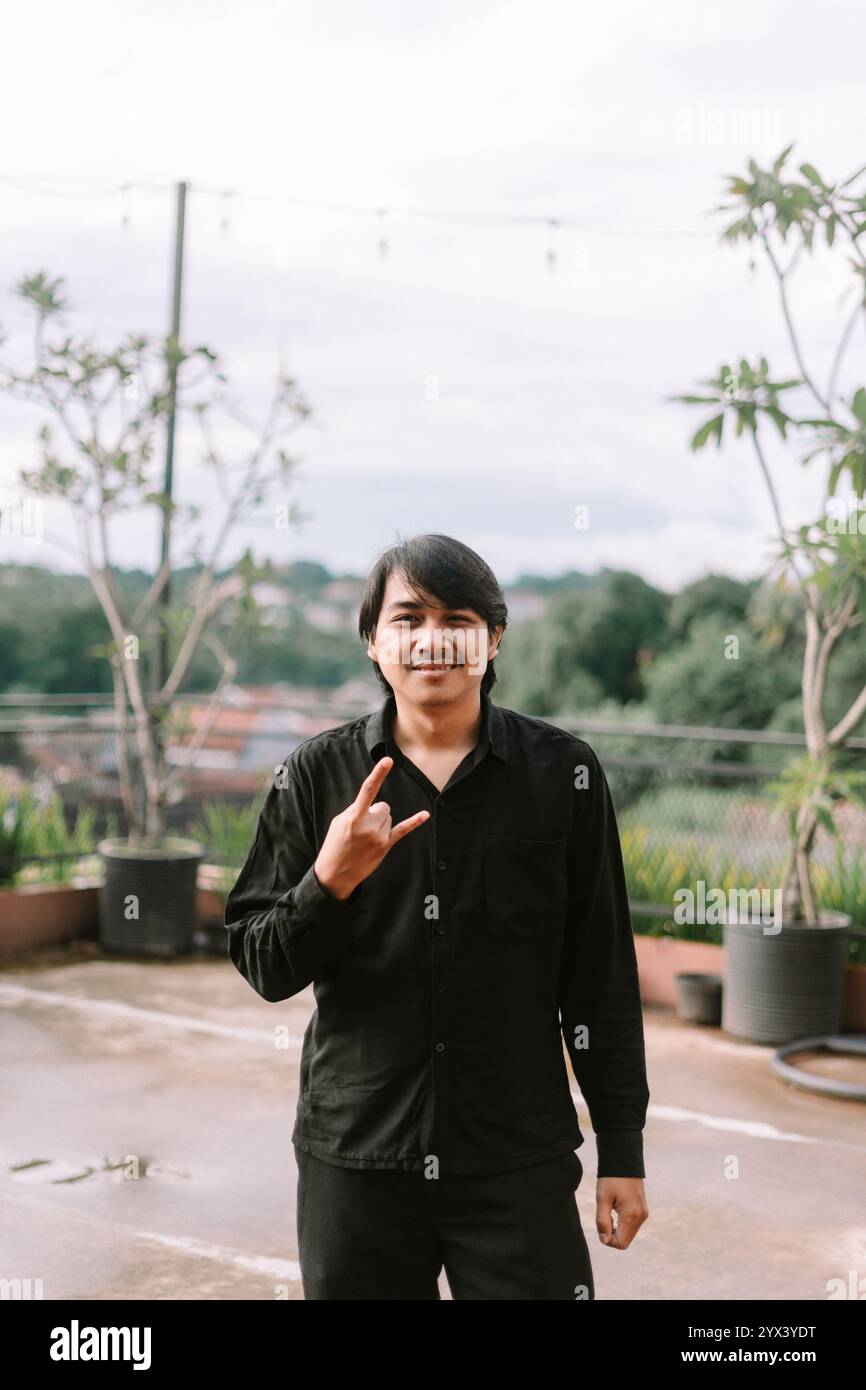 Un homme d'Asie du Sud-est faisant un signe de métal avec ses doigts, exprimant confiance et énergie. Idéal pour la musique, le style de vie ou les projets culturels highlig Banque D'Images