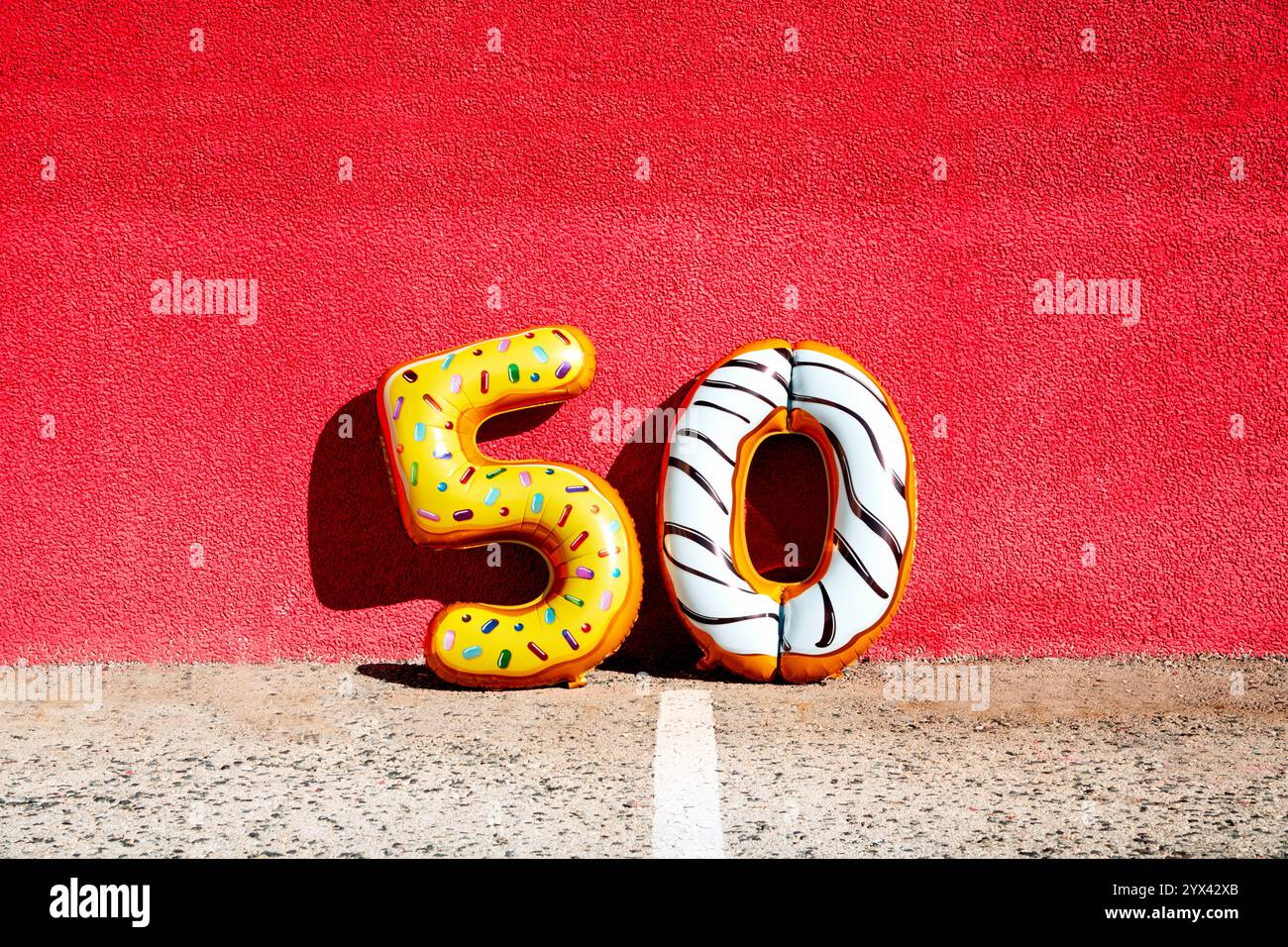 quelques ballons en forme de numéro de feuille de différentes couleurs formant le numéro 50 sur l'asphalte appuyé sur un mur rouge Banque D'Images