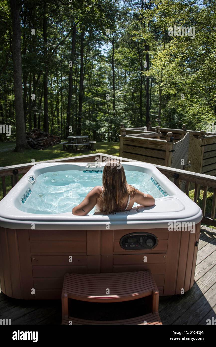 Une femme est vue de derrière, trempée dans un bain à remous luxueux niché au cœur de la forêt à Slade, Kentucky. Entouré de verdure luxuriante et le Banque D'Images