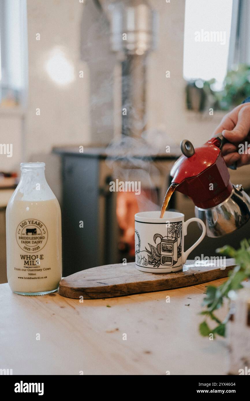 Une personne verse du café dans une tasse à côté d'une bouteille de lait entier. La scène est confortable et accueillante, avec l'arôme de remplissage de café fraîchement moulu Banque D'Images
