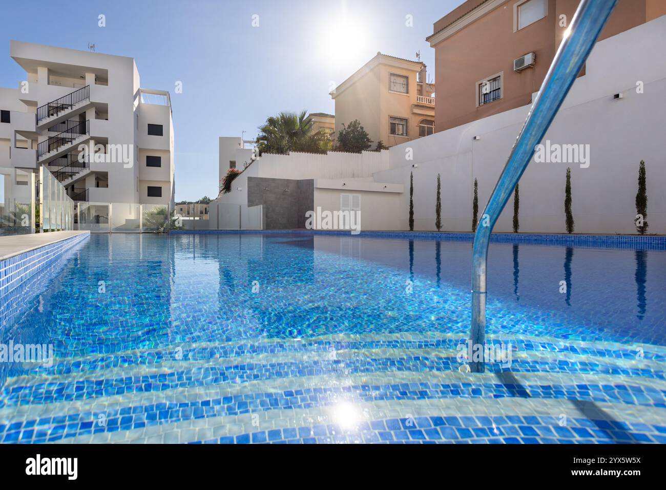 Vue rapprochée d'une piscine cristalline avec marches carrelées, entourée d'un complexe résidentiel moderne et baignée de soleil. Banque D'Images