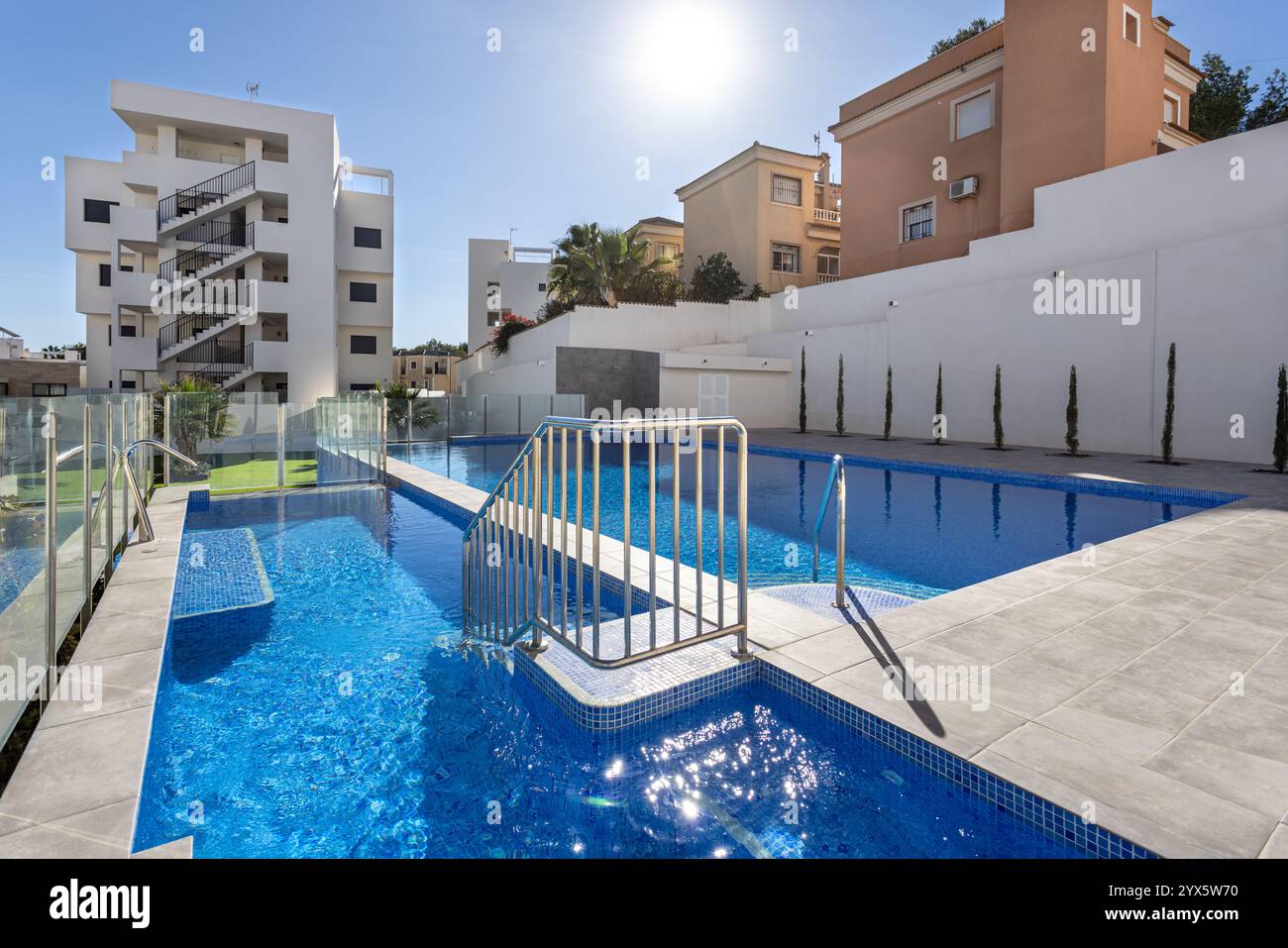 Piscine lumineuse et moderne dotée d'une passerelle centrale, de balustrades en acier inoxydable et entourée de bâtiments résidentiels contemporains et d'espaces paysagers Banque D'Images