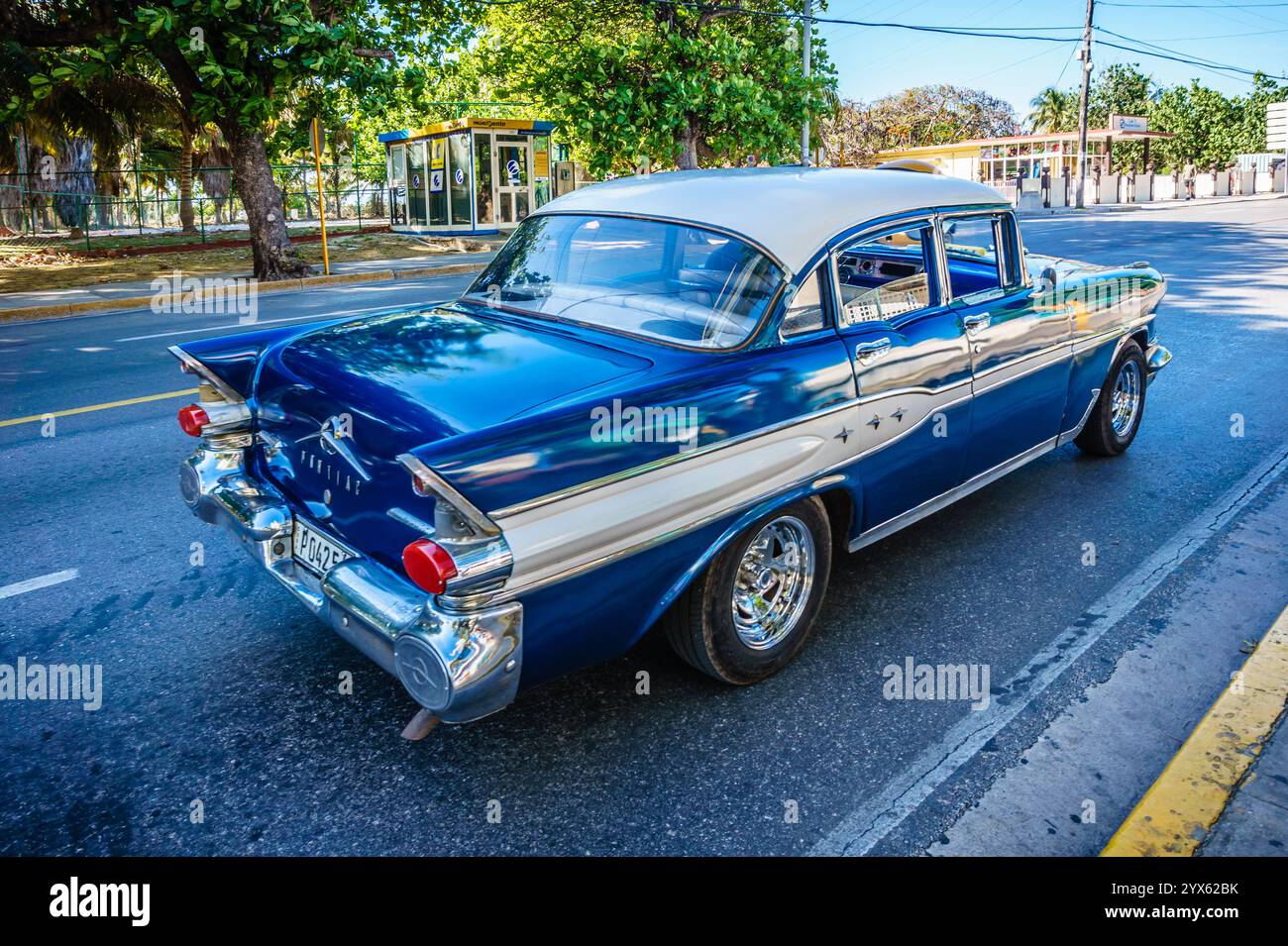 Une voiture bleue et blanche descend une rue. La voiture est ancienne et a un design classique. La scène est nostalgique et rappelle une époque révolue Banque D'Images