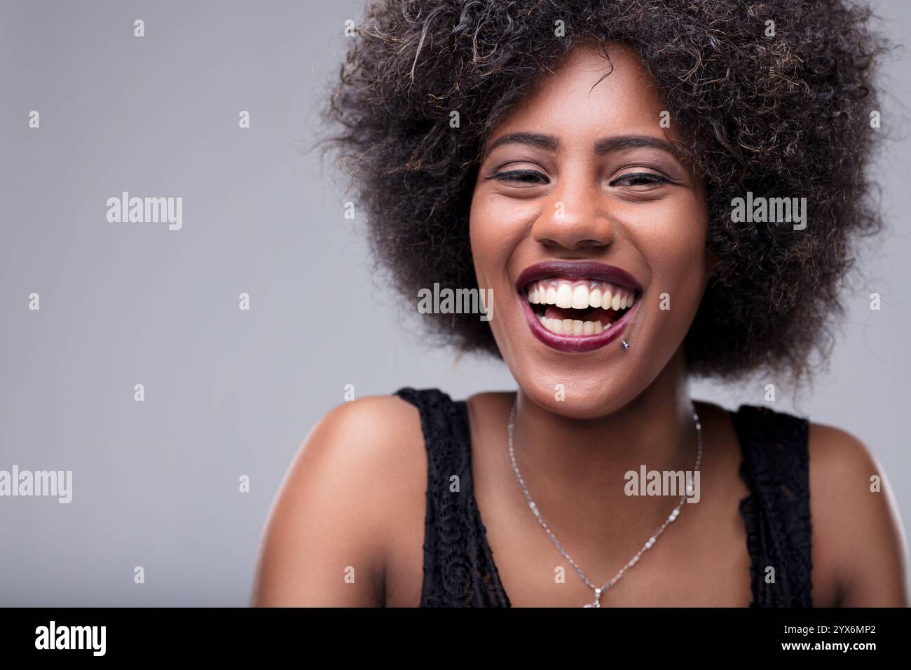 Portrait studio mettant en scène une jeune femme joyeuse aux cheveux afro, souriant largement et révélant ses dents, rayonnant de bonheur et de joie dans une exp vibrante Banque D'Images