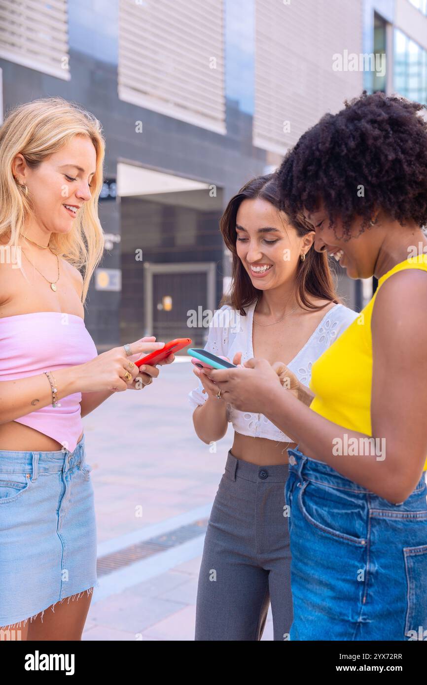 Trois amis enthousiastes regardant un smartphone à l'extérieur. Vertical Banque D'Images
