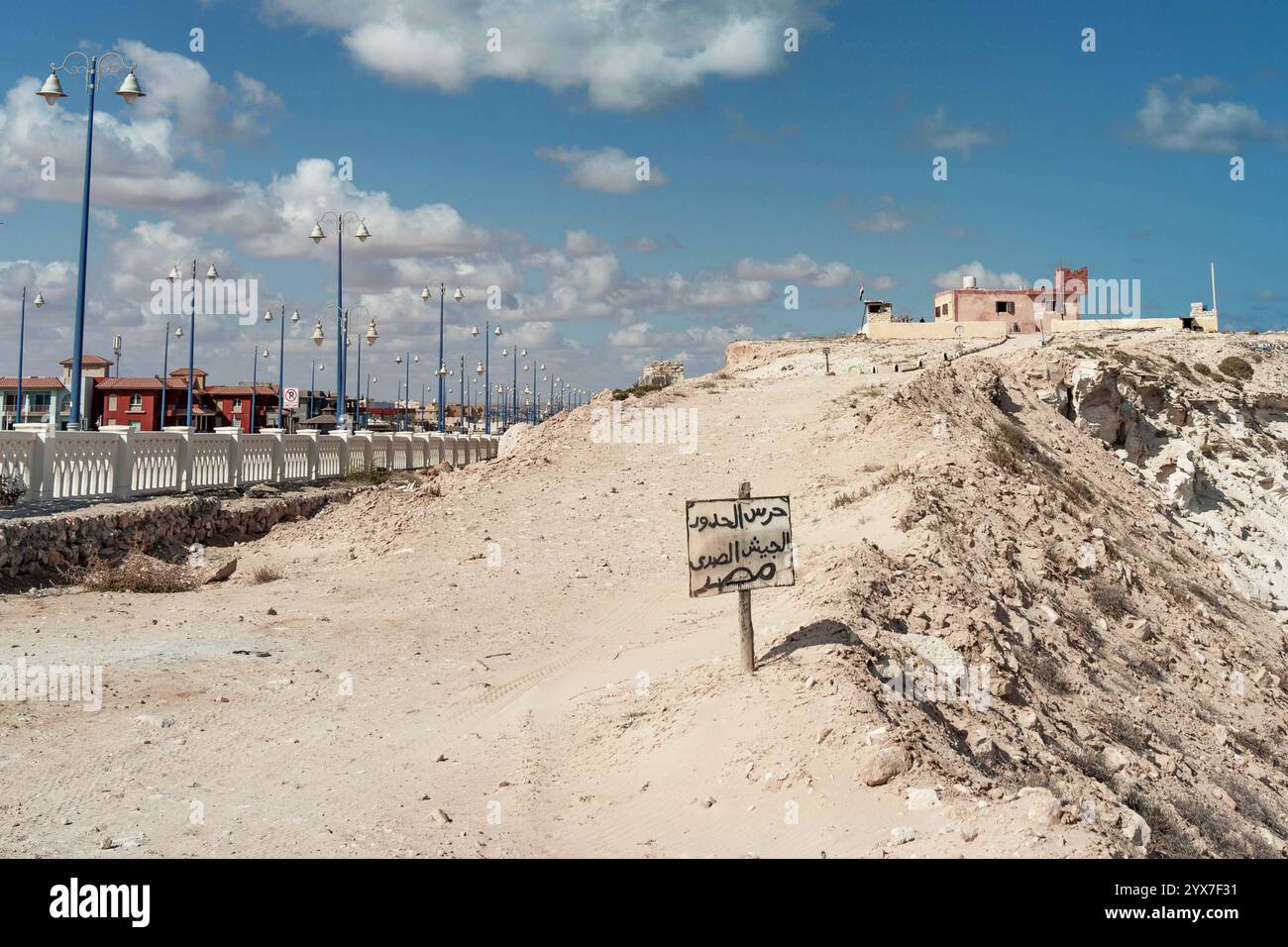 Une vue panoramique sur la côte de Mersa Matruh avec un paysage désertique accidenté, un panneau militaire égyptien à la frontière et des rangées de lampadaires modernes. Banque D'Images