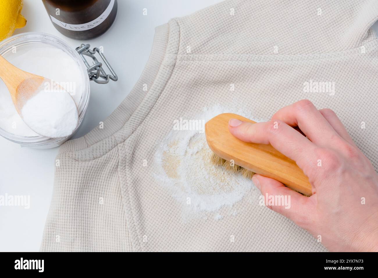 Une main de personne à l'aide d'une petite brosse frottant la poudre de bicarbonate de soude sur une tache jaune sur les vêtements ou les tissus d'ameublement. Produits naturels pour enlever les taches. vue de dessus Banque D'Images