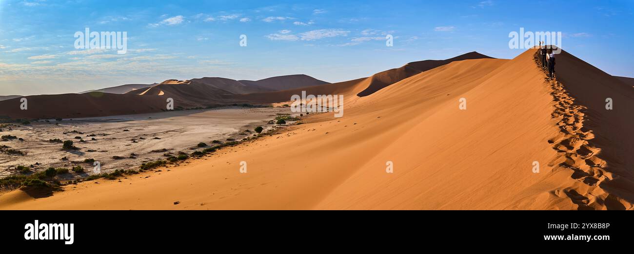 Sossusvlei est vu depuis la crête d'une dune. Les gens marchant le long de la crête laissent des empreintes de pas. Parc national de Sesriem, Namibie, Afrique. Banque D'Images