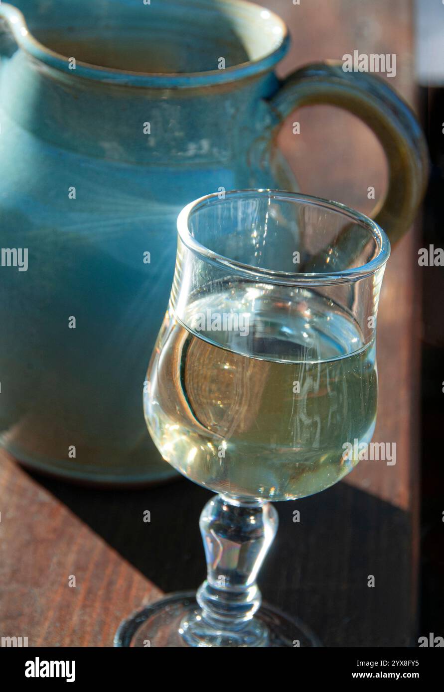 Vin blanc et carafe en porcelaine rustique sur la table ensoleillée, vin blanc de pays français simple sur la table ensoleillée du Gite de France avec carafe en faïence bleue derrière en plein soleil. France Banque D'Images