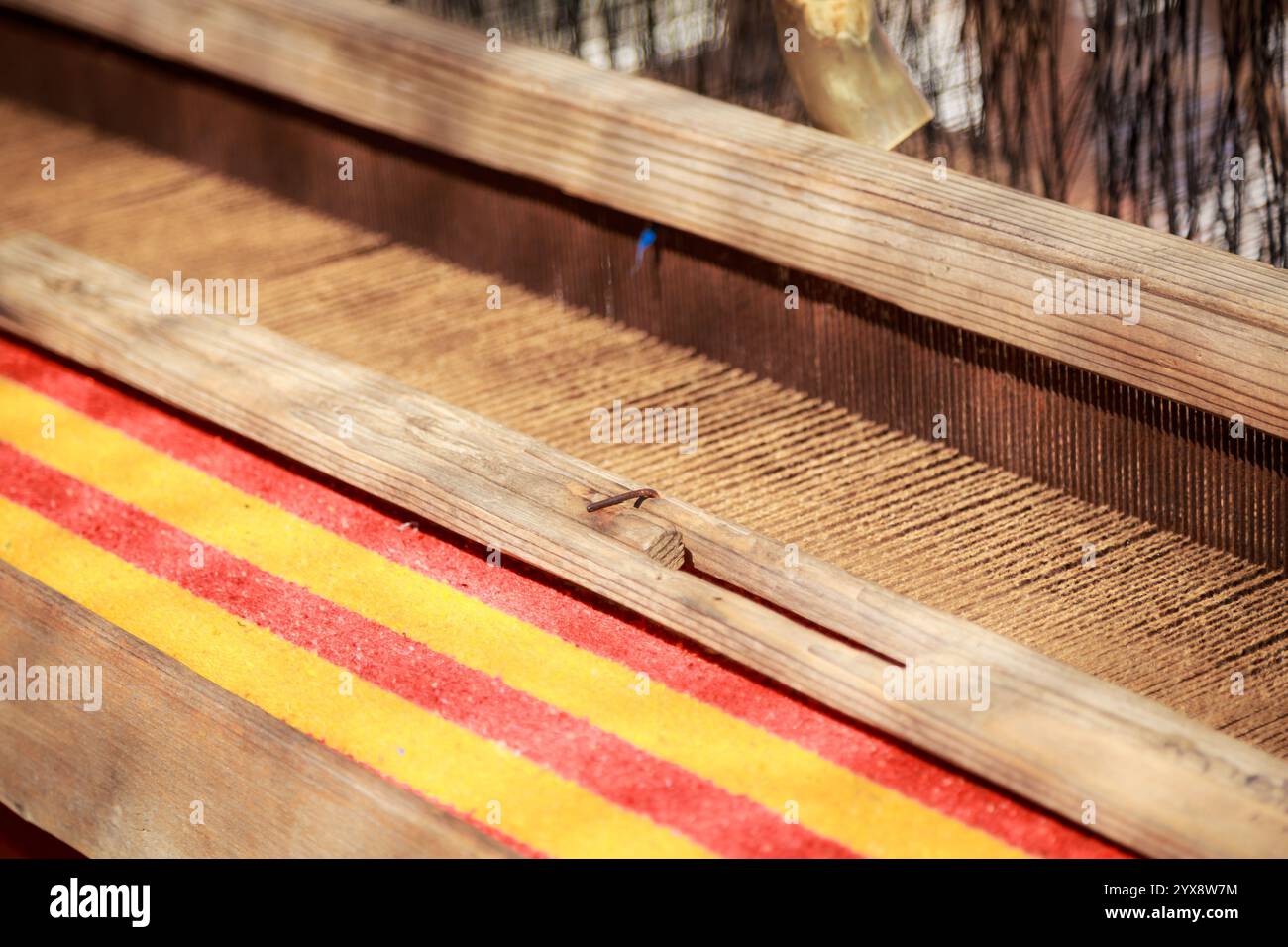 Une planche de bois avec un tapis rayé rouge et jaune en dessous. Le tapis est tissé par une machine Banque D'Images