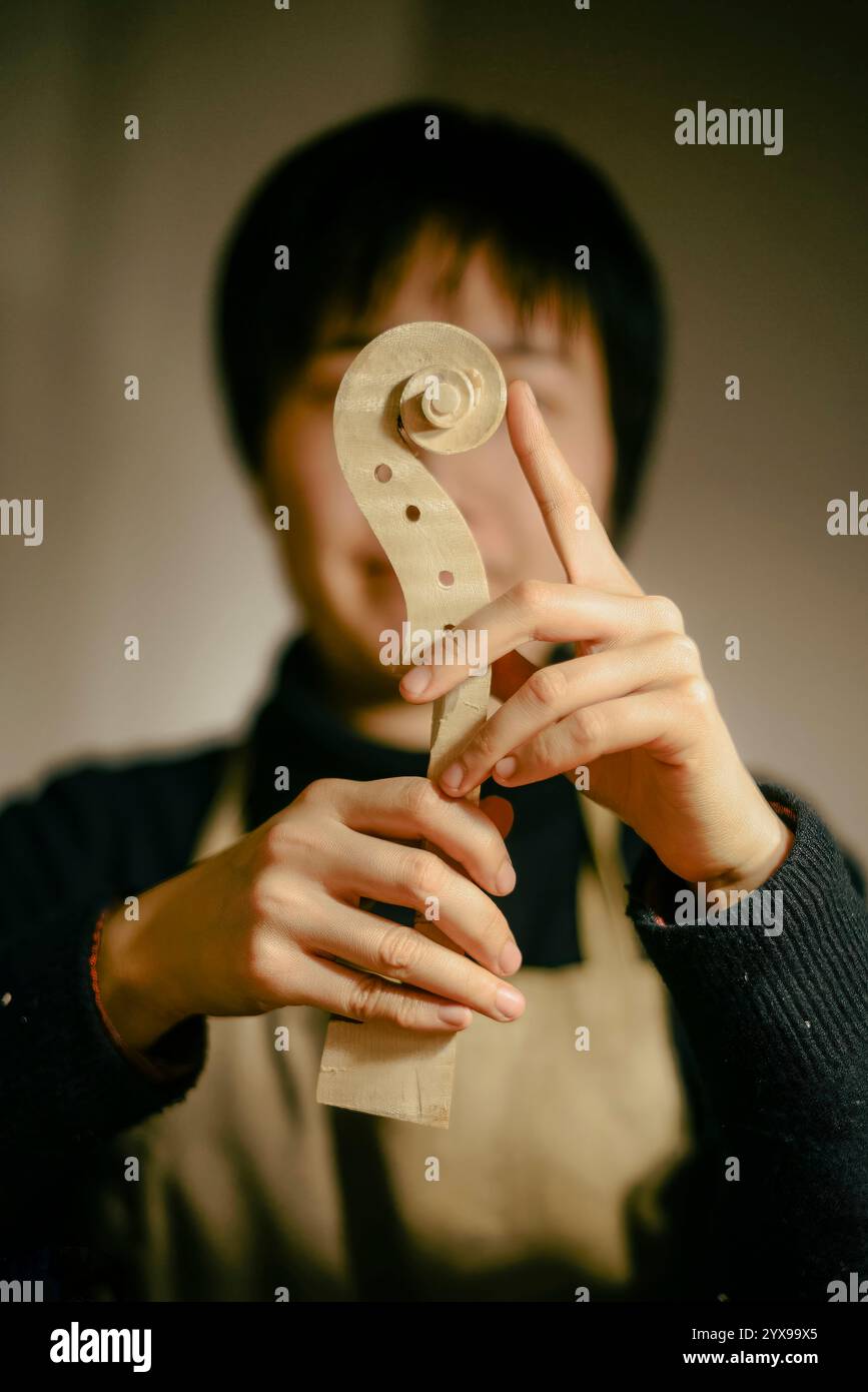 Luthier travaillant sur un nouveau violon, examinant attentivement le rouleau du cou, vérifiant sa forme parfaite et sa finition lisse, fier de l'artisanat et Banque D'Images