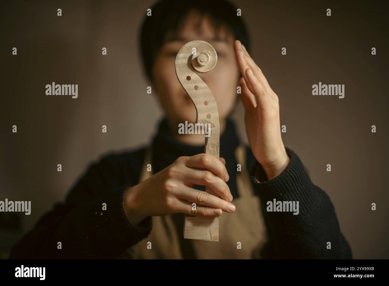 Luthier féminin asiatique examinant soigneusement un cou de violon fabriqué à la main dans son atelier, en se concentrant sur l'obtention d'une forme et d'une qualité parfaites grâce à la cr qualifiée Banque D'Images