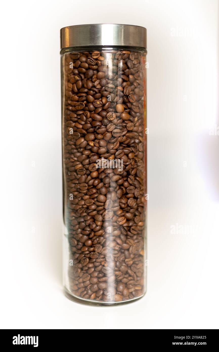 Un grand récipient en verre rempli de grains de café torréfiés brillants se dresse sur un fond neutre, ajoutant une touche d'élégance à n'importe quelle cuisine. Le bea Banque D'Images