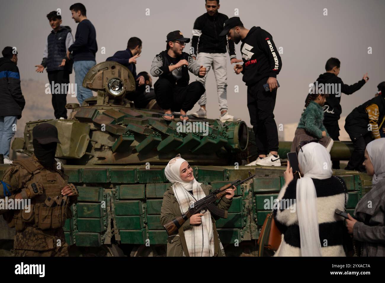 FILE - A woman holding a rifle borrowed from a Syrian opposition fighter poses for a picture next to a government forces tank that was left on a street at Umayyad Square in Damascus, Syria, Wednesday, Dec. 11, 2024. (AP Photo/Leo Correa, File) Banque D'Images
