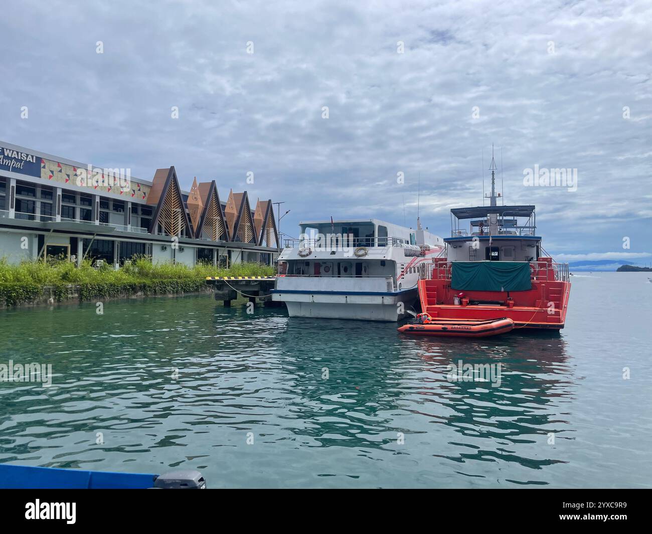 Port de Waisai à l'architecture moderne, deux bateaux amarrés - un blanc, un rouge - et un petit canot de sauvetage sur des eaux calmes sous un ciel nuageux., Waisai, Raja Amp - Image de stock capturée avec un smartphone