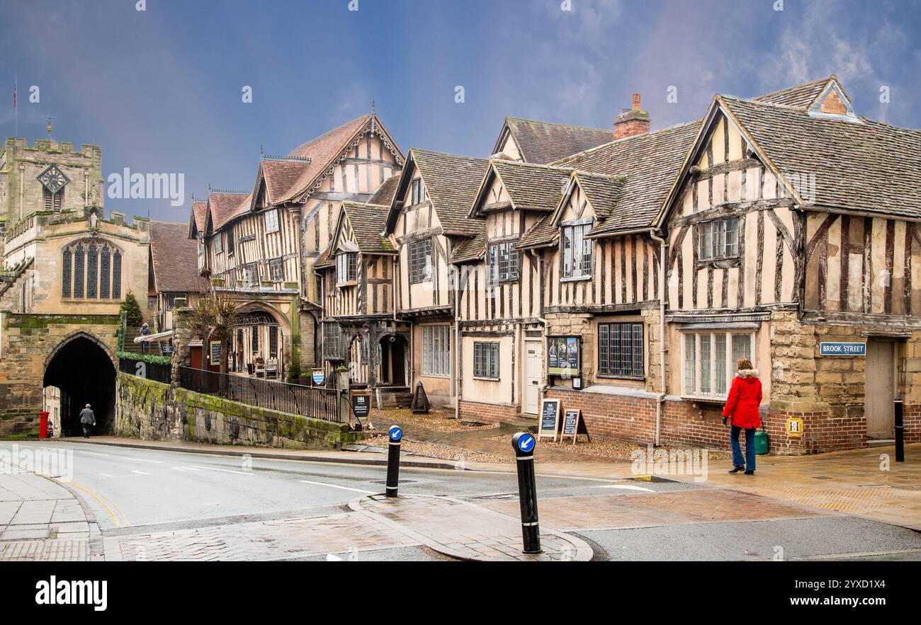 Femme en manteau rouge marchant devant l'hôpital médiéval Lord Leycester, un organisme de bienfaisance soutenant les anciens militaires et les femmes dans la ville de Warwick dans le Warwickshire Banque D'Images