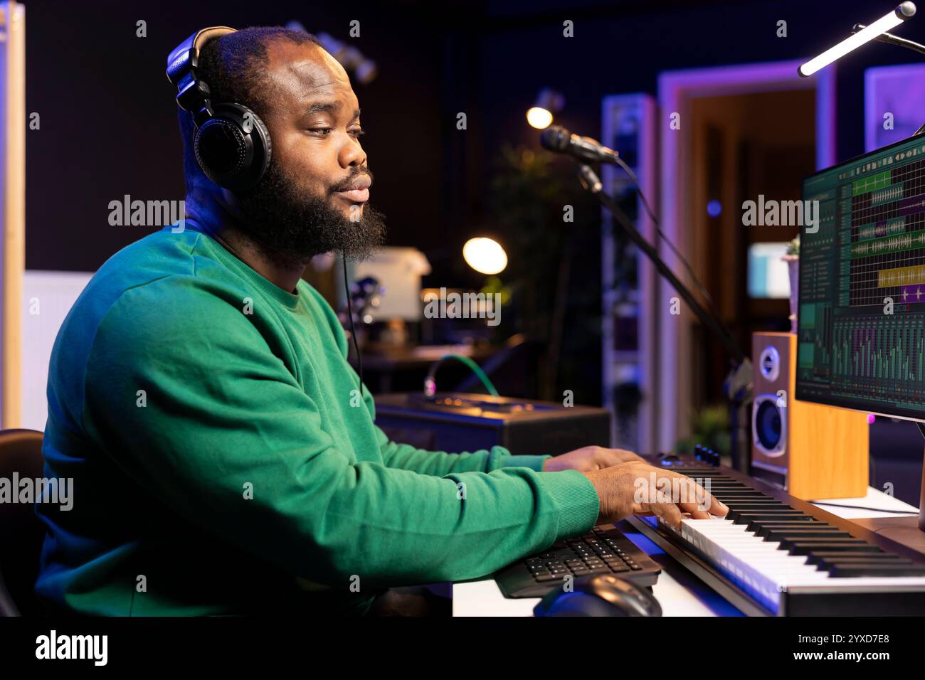 Artiste afro-américain compositeur jouant un clavier électronique pour enregistrer l'acoustique sur un logiciel professionnel et ajouter des effets sonores. Ingénieur du son éditant des bandes sonores avec console stéréo et outils. Banque D'Images