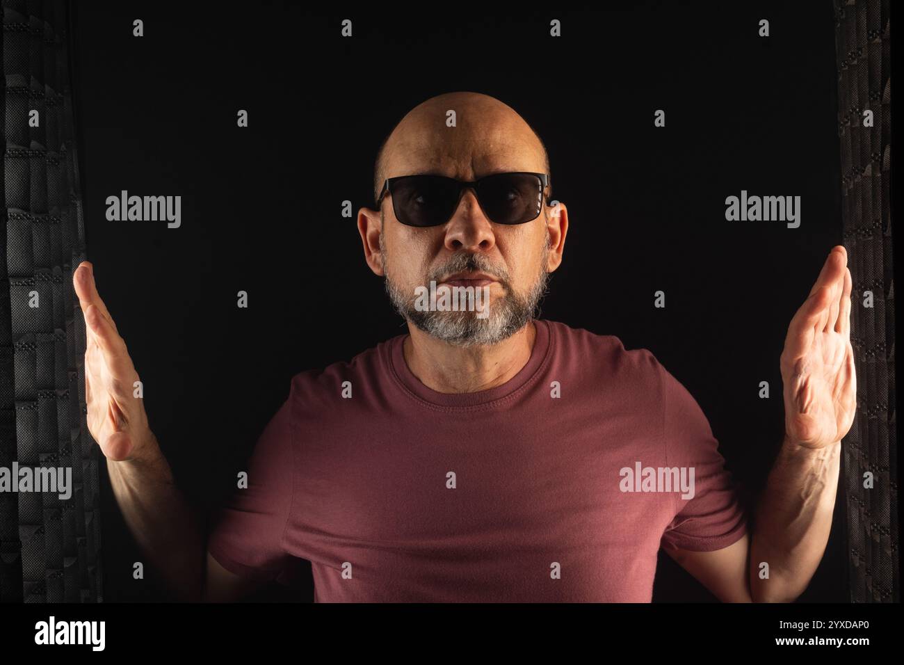 Homme chauve et barbu portant des lunettes de soleil avec les mains levées. Isolé sur fond fumé foncé. Personne sud-américaine. Banque D'Images