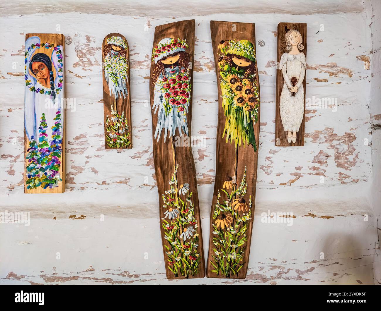 Sanok, Pologne - 4 mai 2024. Cinq plaques en bois peintes à la main représentant des anges fantaisistes et des filles de fleurs accrochées sur un fond rustique en bois blanc. Banque D'Images