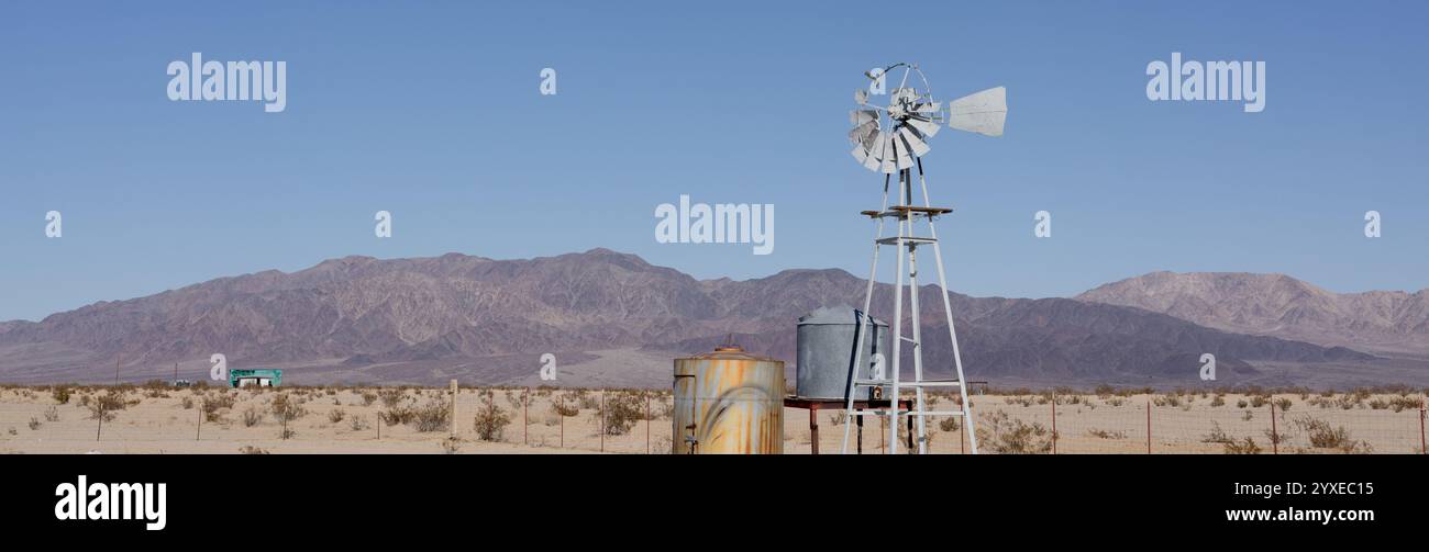 Une pompe à eau rustique moulin à vent se trouve dans le désert aride de 29 Palms' Wonder Valley, encadrée par de vastes montagnes et un ciel ouvert Banque D'Images