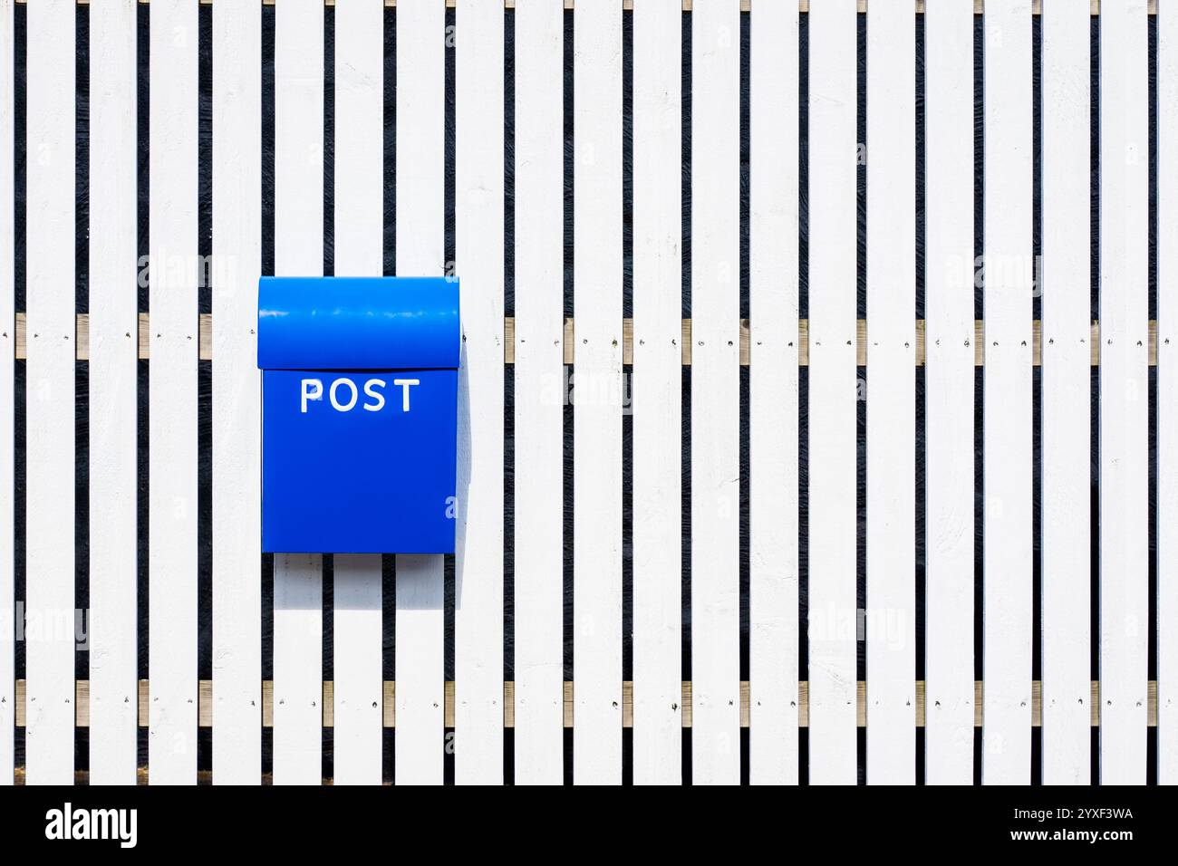 Vue de face d'une boîte aux lettres en plastique bleu portant l'inscription « post » en majuscules blanches attachée à une clôture en bois blanche. Banque D'Images